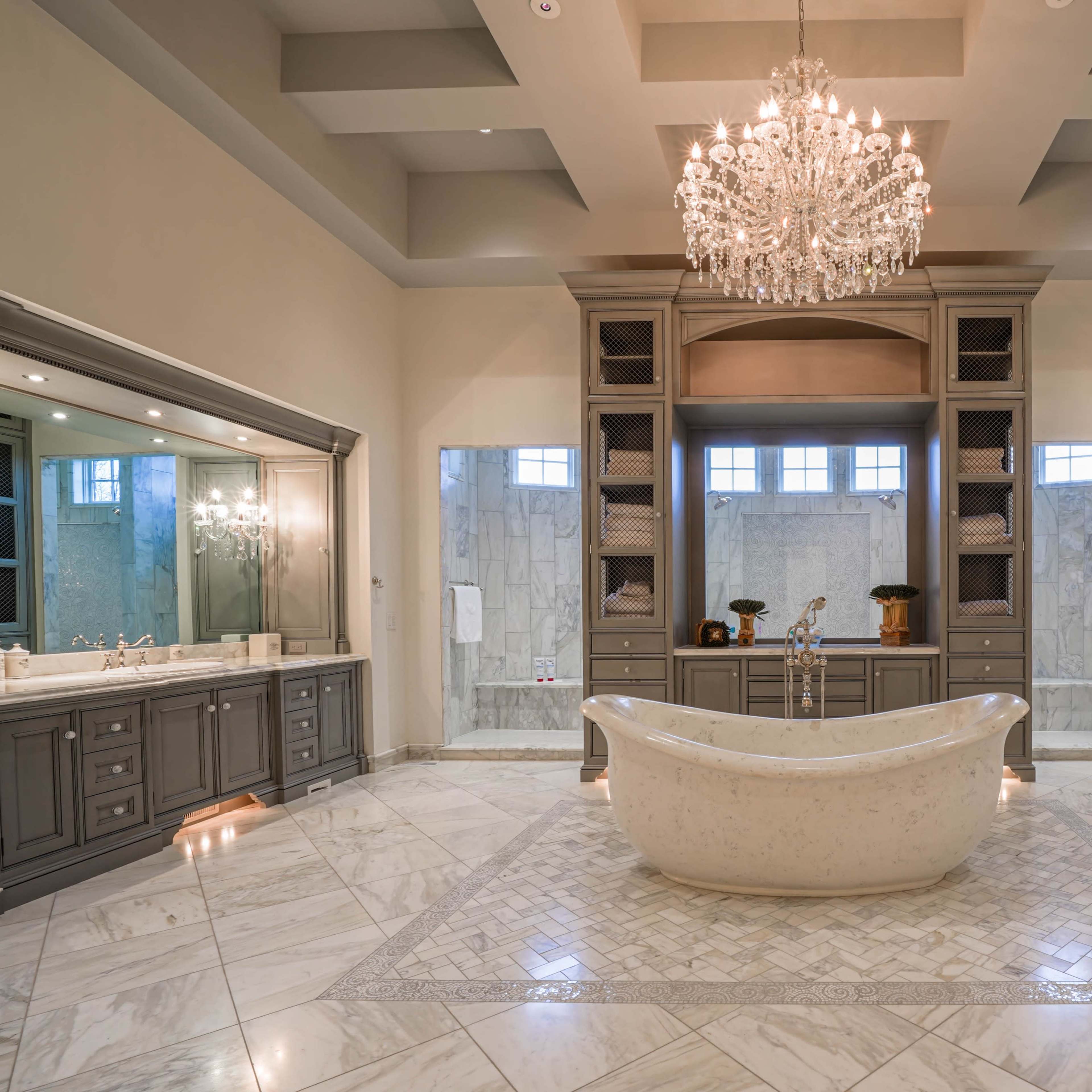 A luxurious bathroom featuring a central freestanding bathtub, dual sinks with large mirrors, and a chandelier above in a spacious layout with marble flooring.