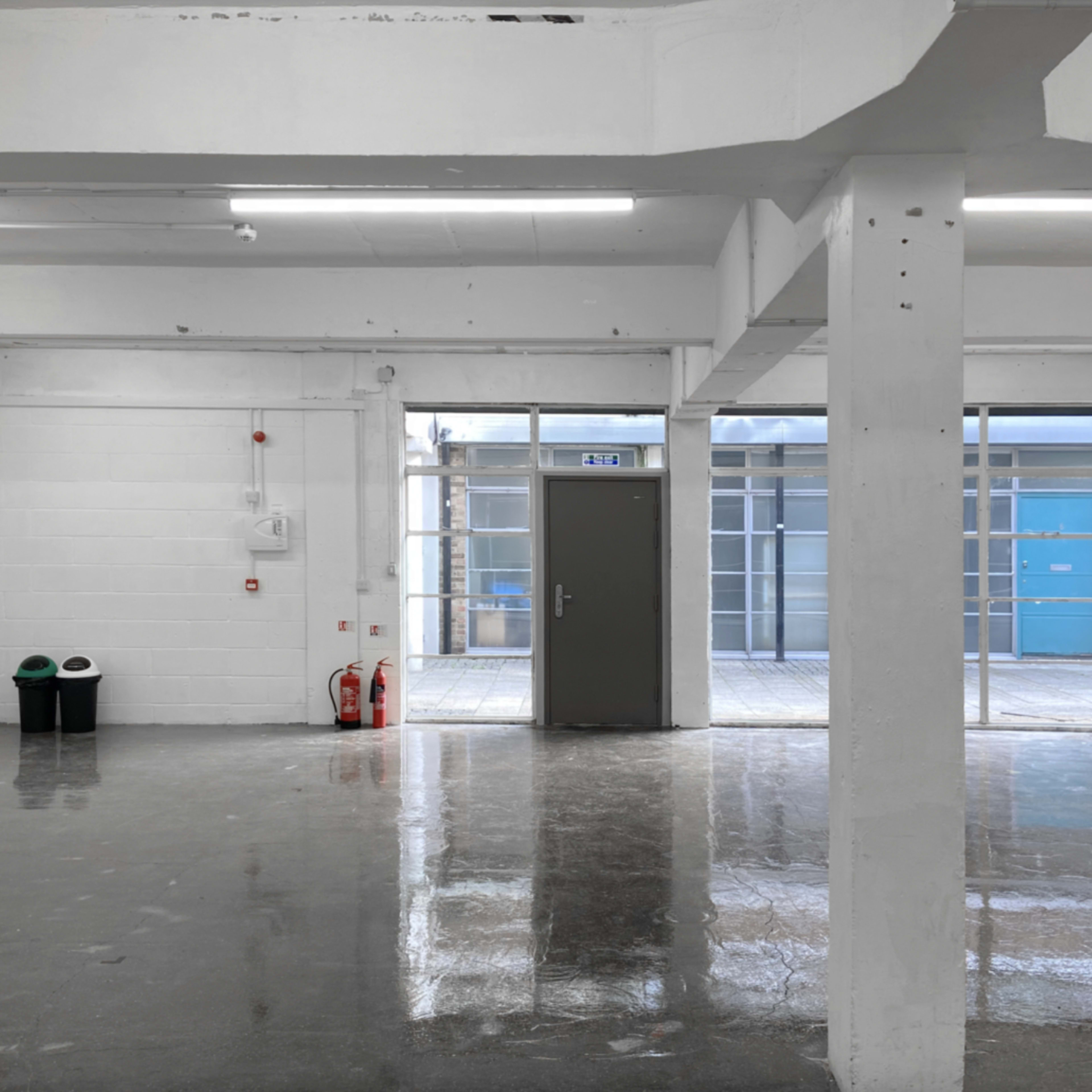A large, empty, well-lit room with polished concrete floors and a door leading to an outdoor area.