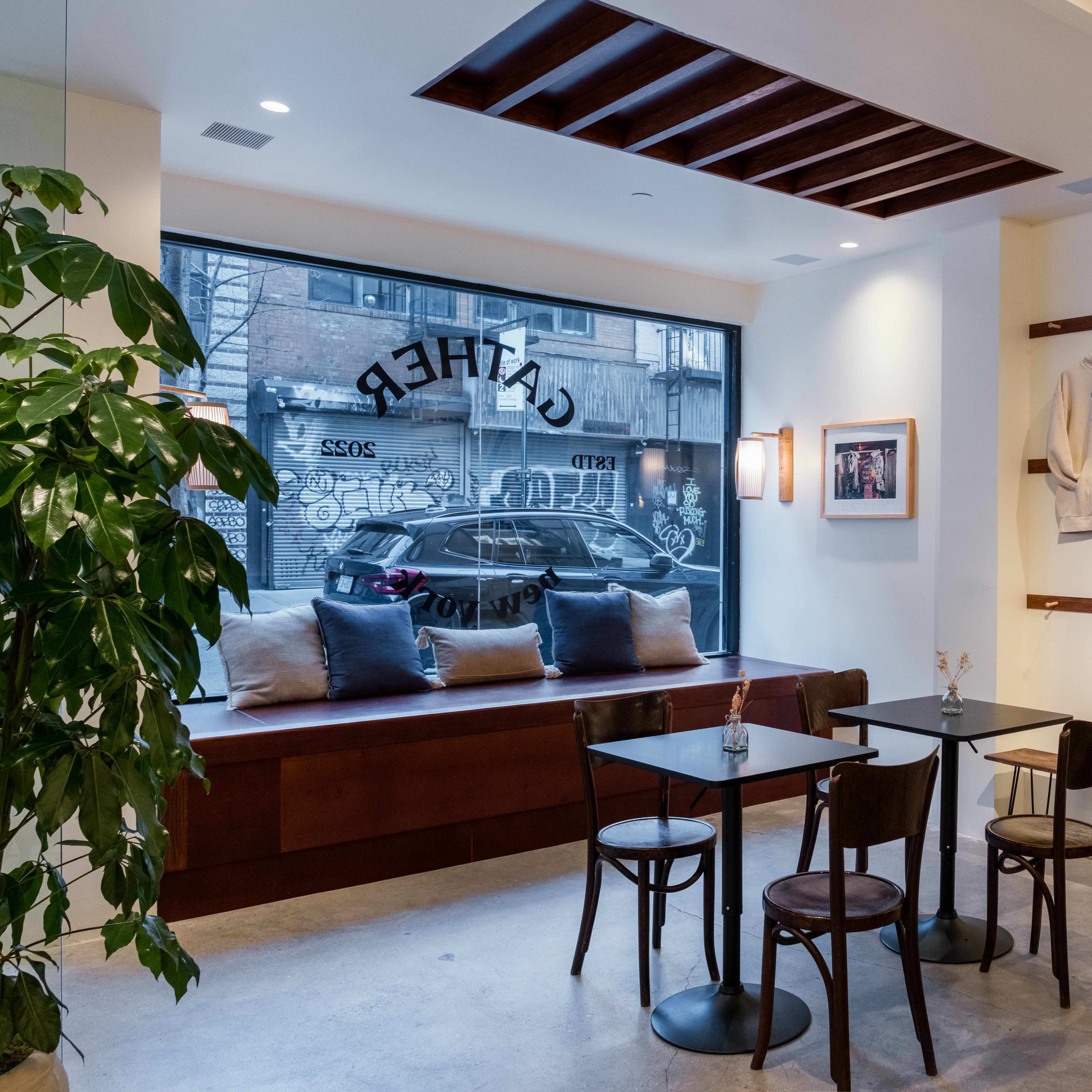 A modern cafe interior with a large window, minimalist furniture, and a wooden bench along the wall.