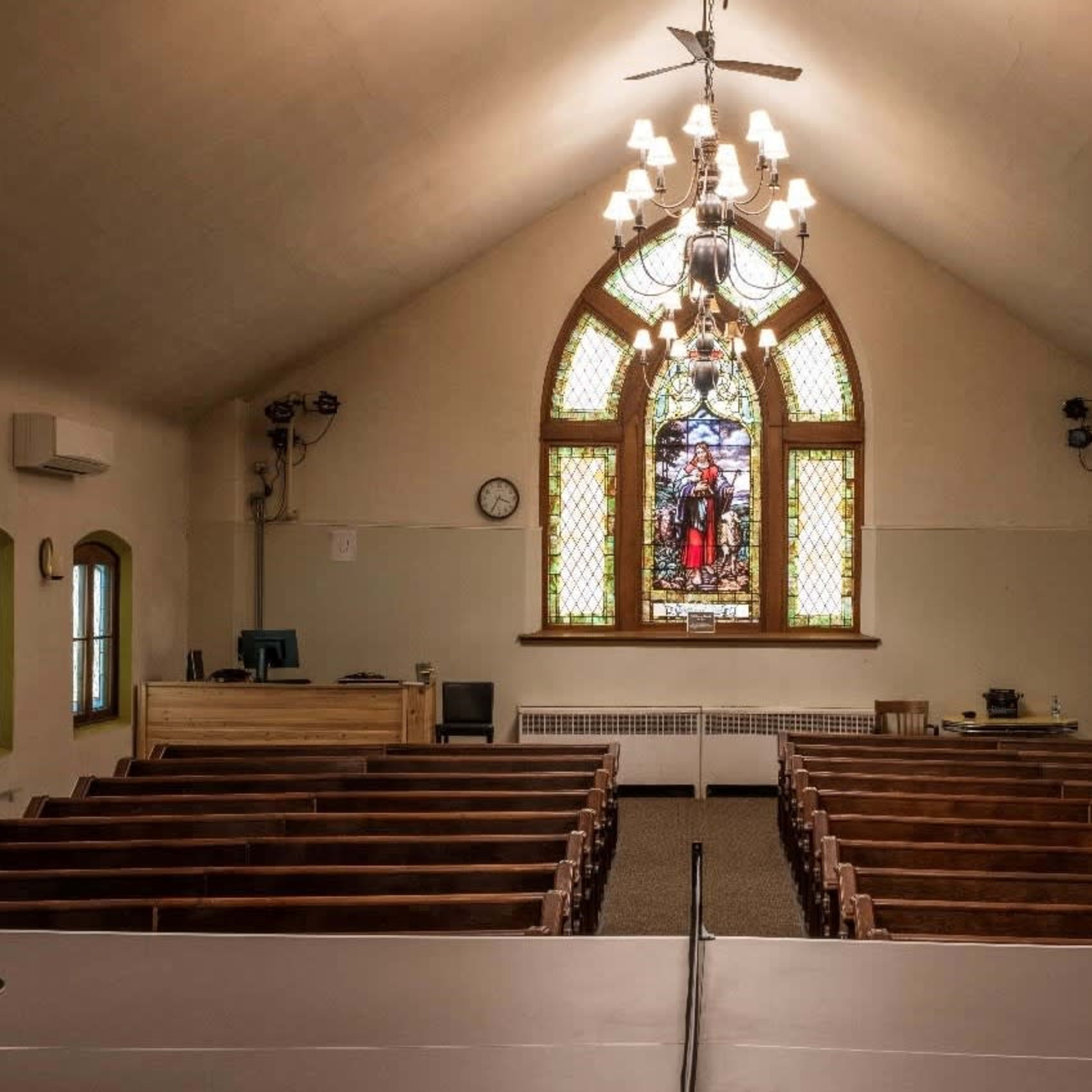 The interior of a church with wooden pews facing a stained glass window at the front.
