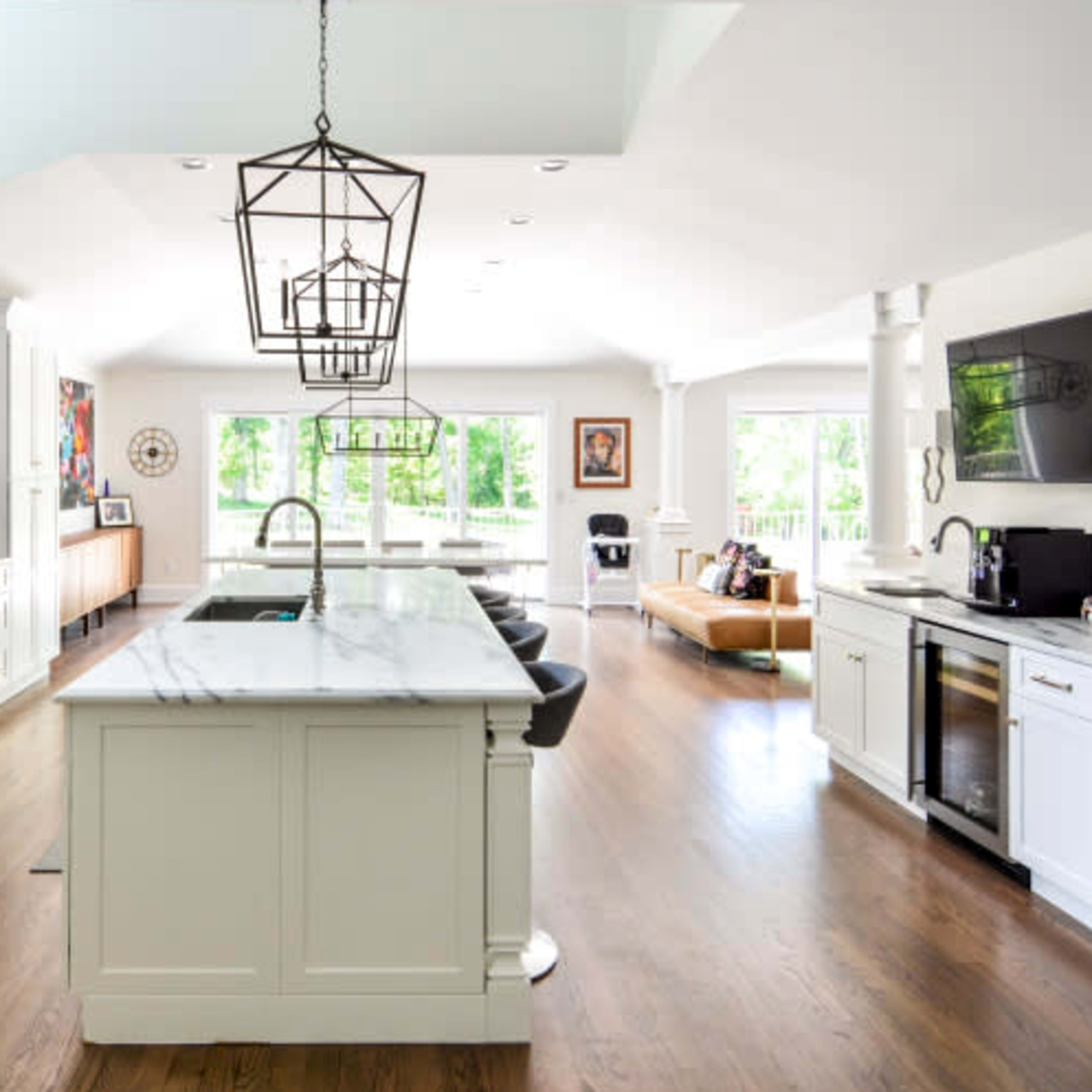 A modern kitchen with white cabinets, a large marble island, and an open layout that connects to a living area filled with natural light.