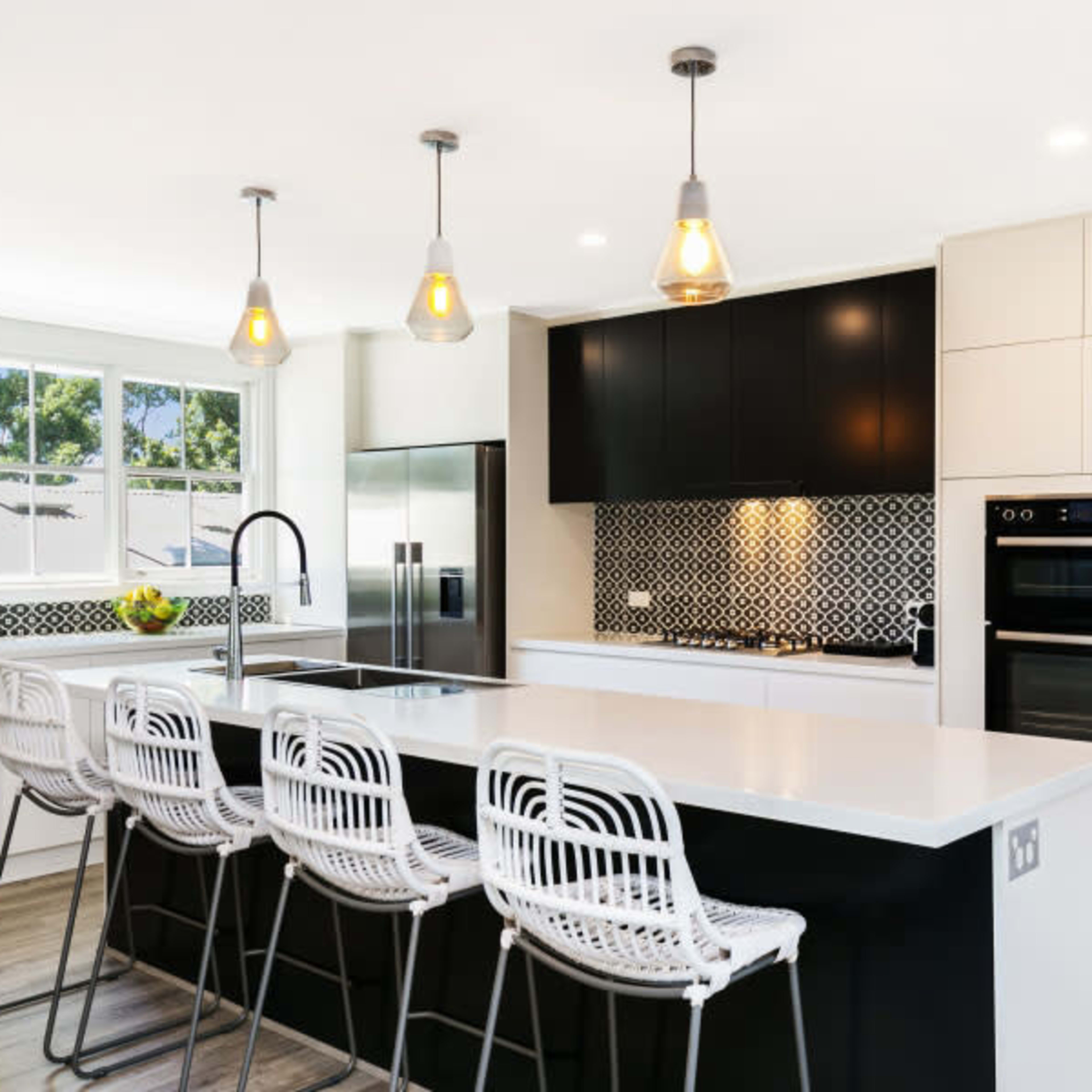 A modern kitchen with a large island featuring bar stools, sleek cabinetry, and decorative tile backsplash.