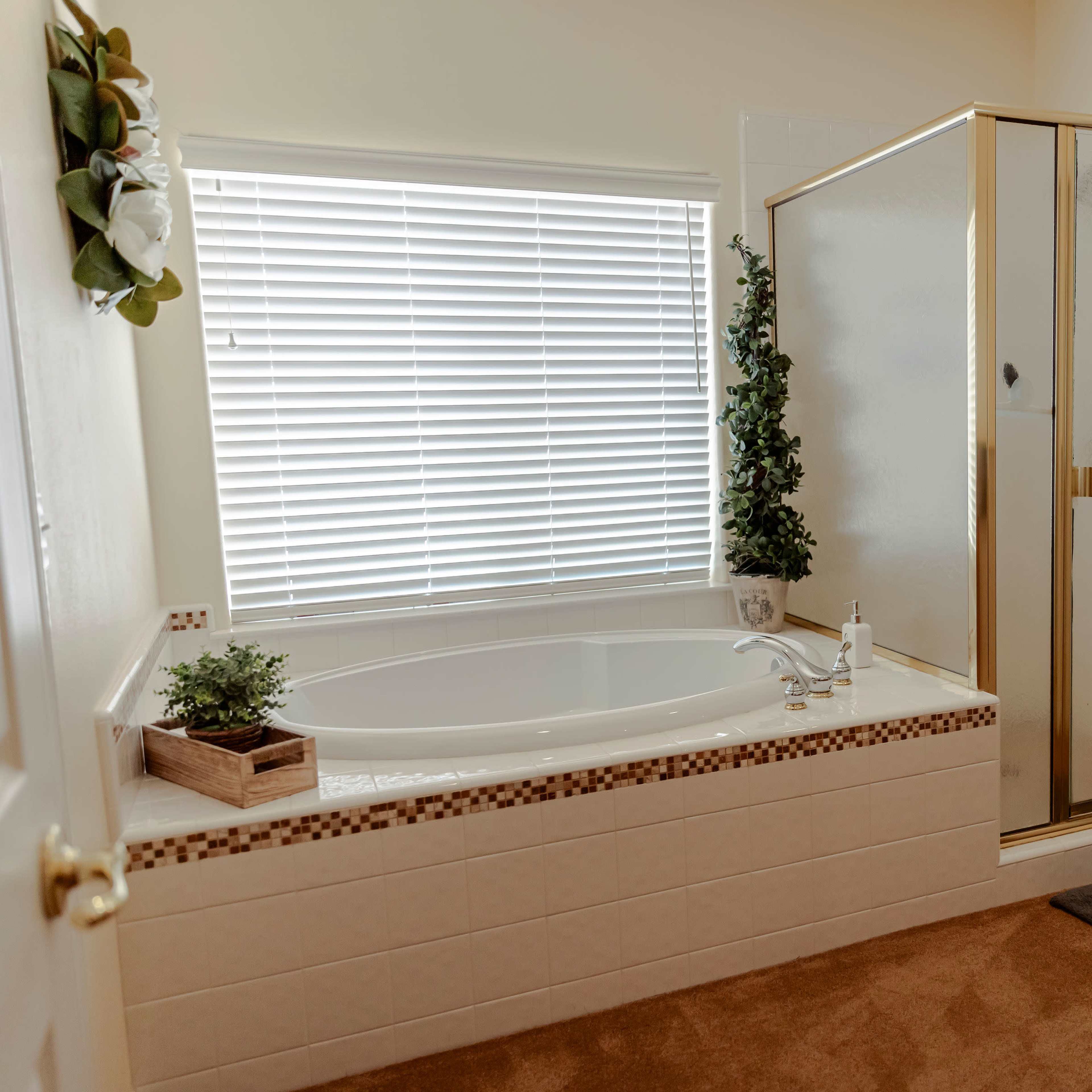 The bathroom features a corner bathtub, a glass shower enclosure, and a double sink vanity with a tan countertop.