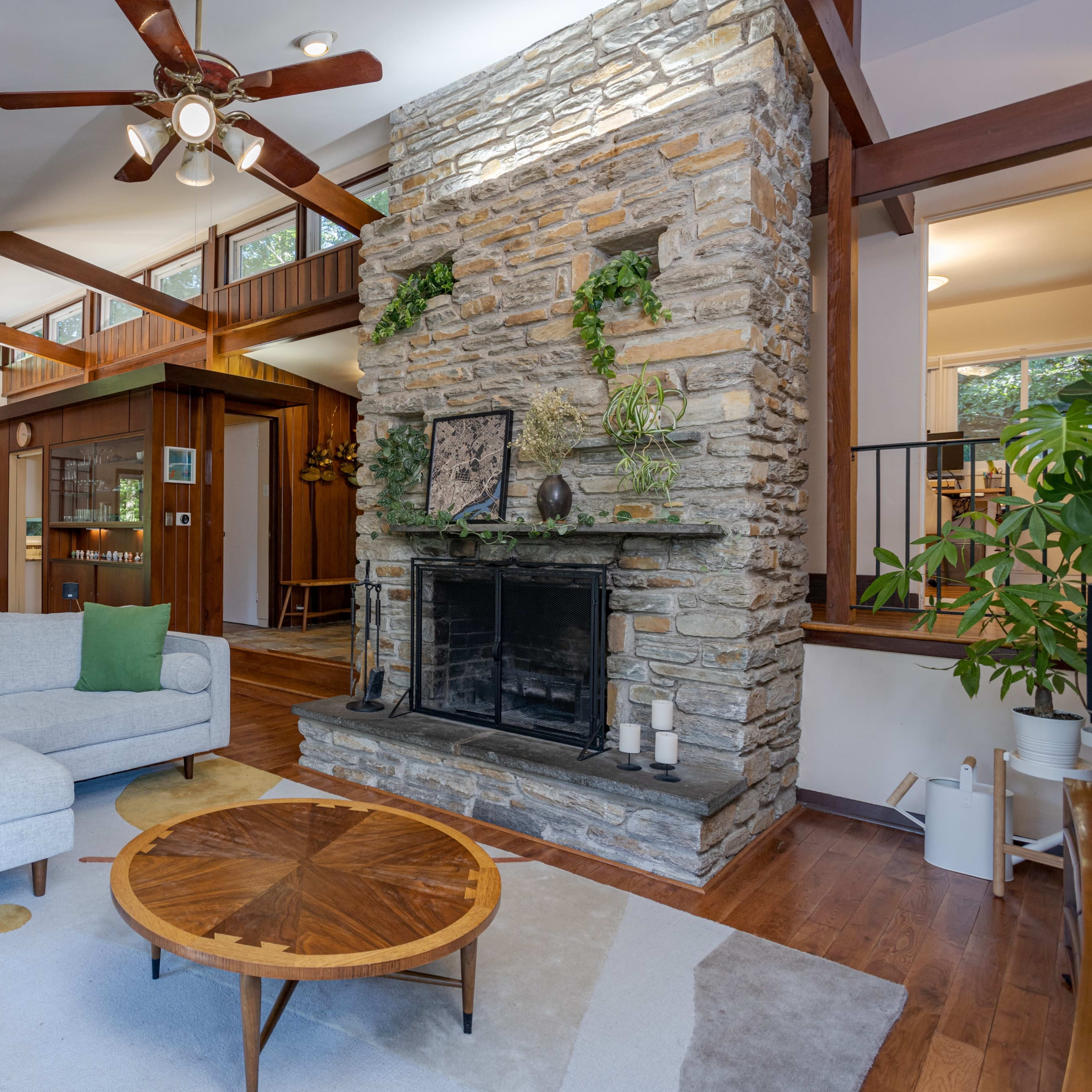 A cozy living room featuring a stone fireplace, wooden accents, and a light-colored sofa facing a round coffee table.
