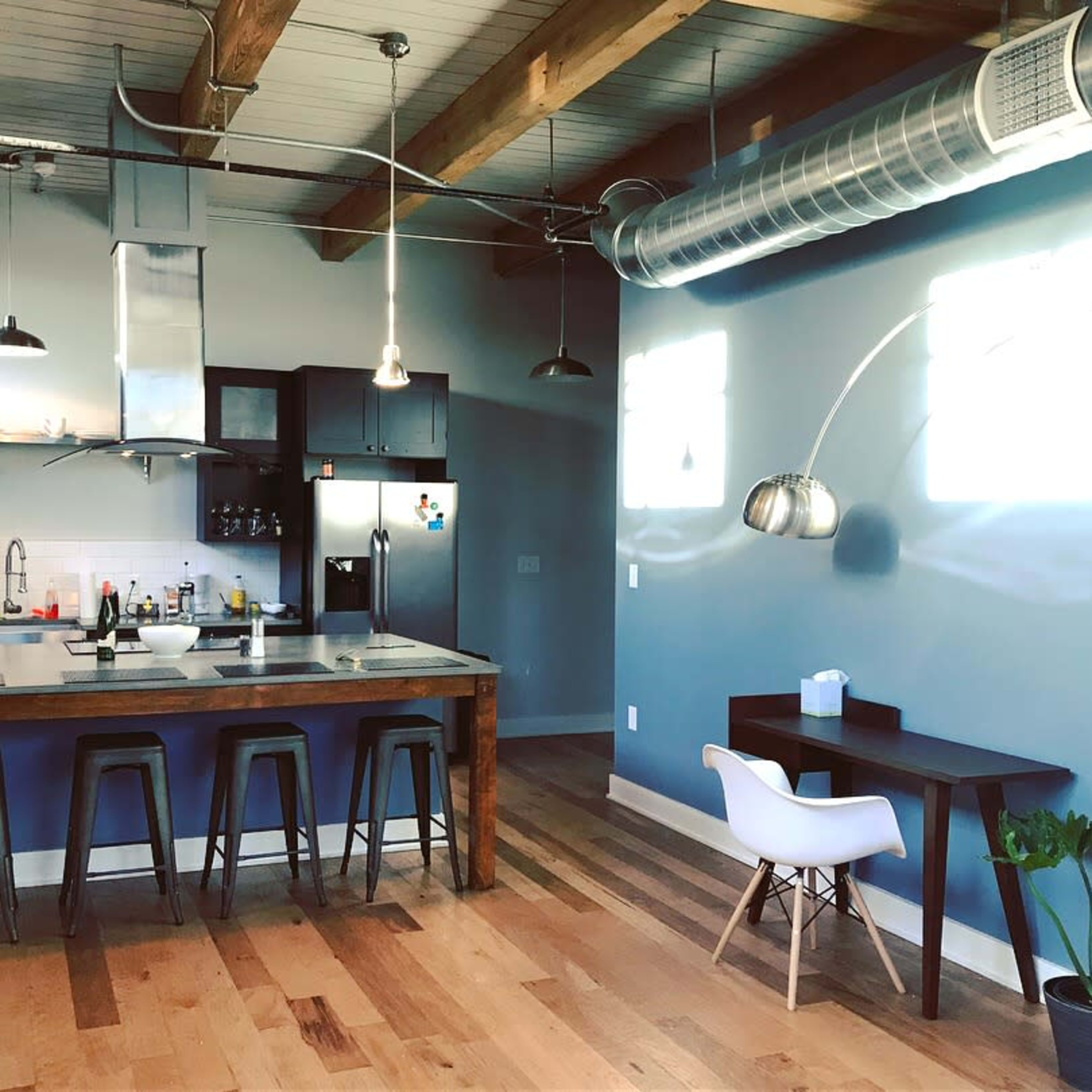 A modern kitchen with a large island, wooden floors, and industrial-style lighting.