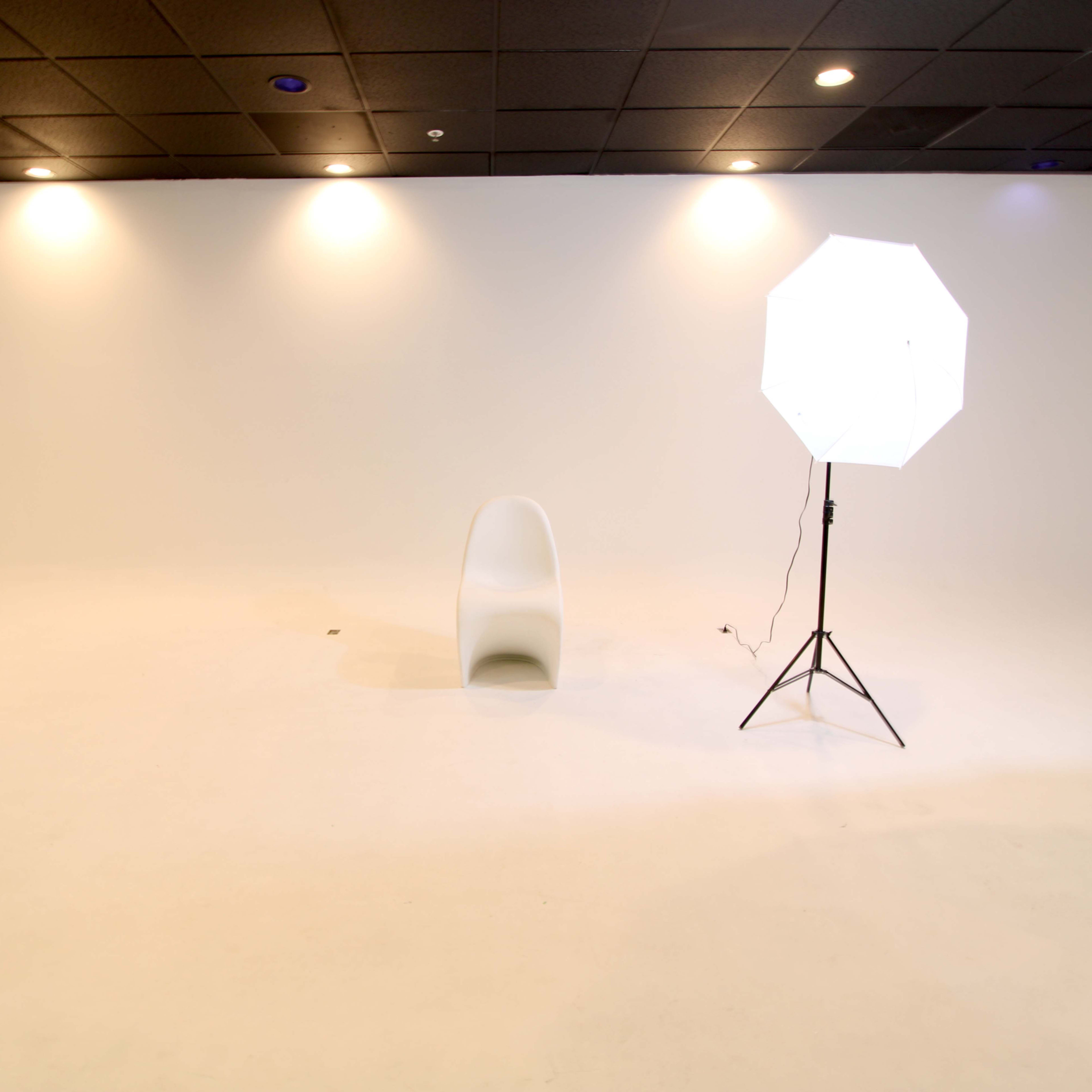 A minimalistic white studio space with a single chair and a lighting setup.