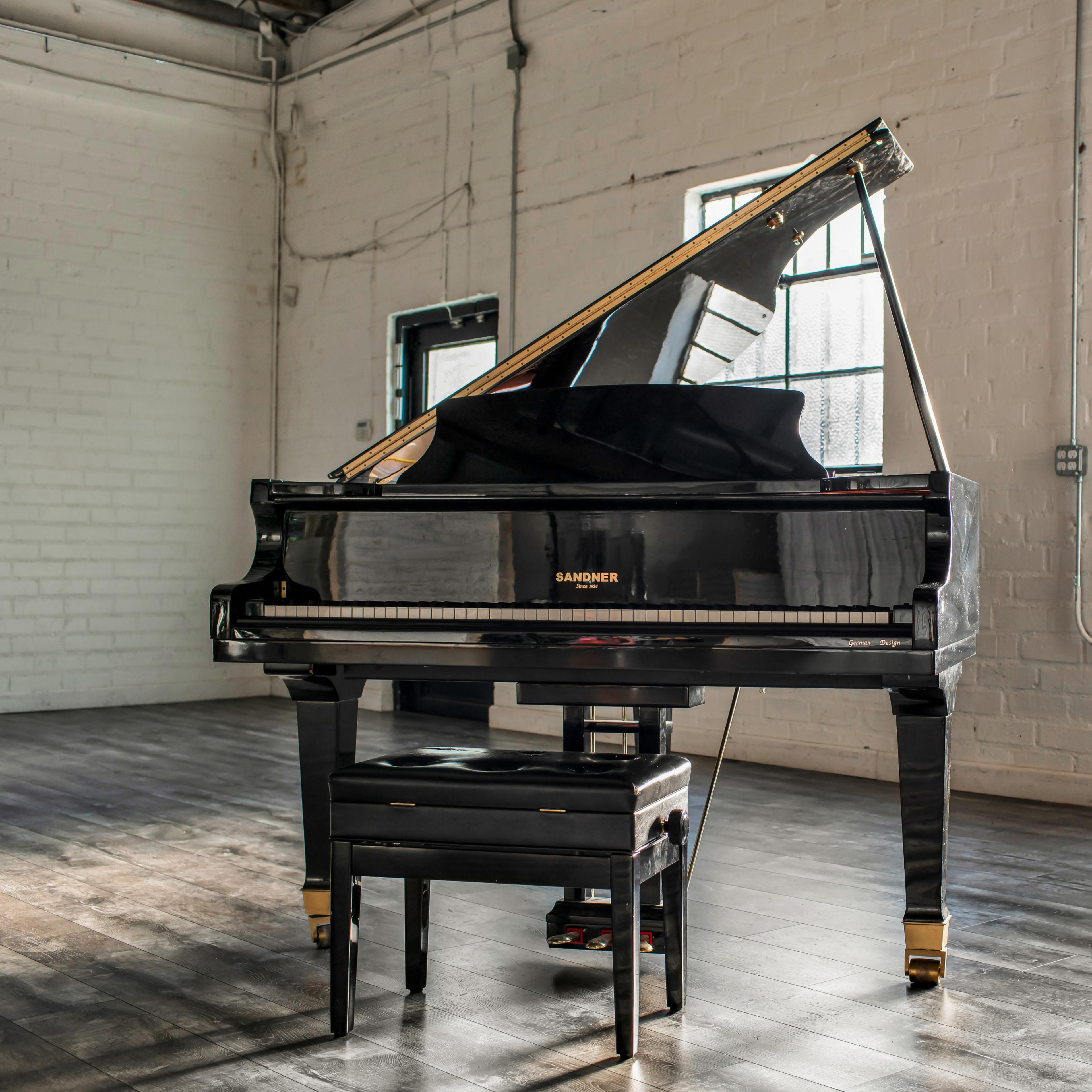 A grand piano with an open lid is positioned in a bright, airy room with large windows and polished wooden floors.