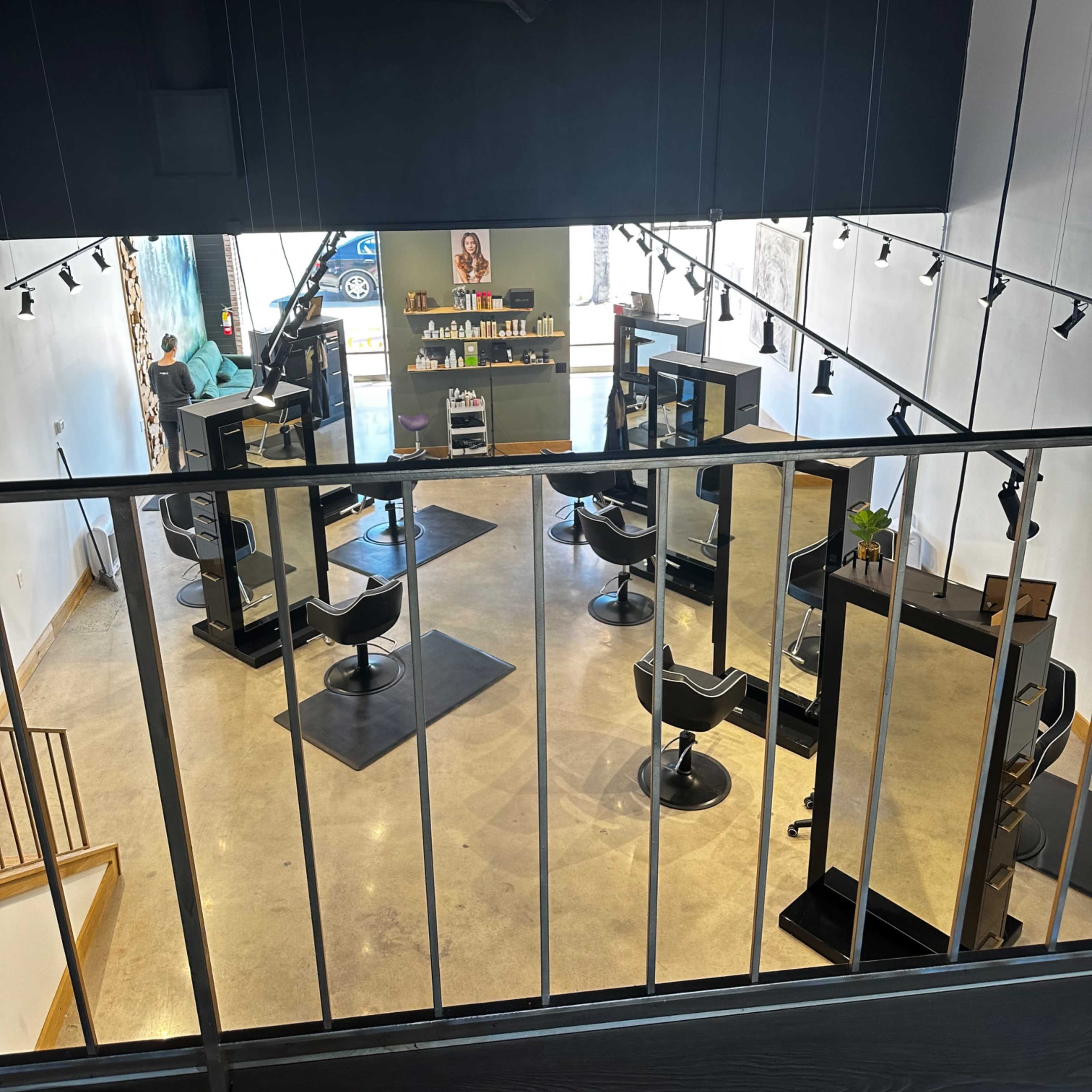 A brightly lit hair salon with several styling stations, mirrors, and a staircase in the foreground.