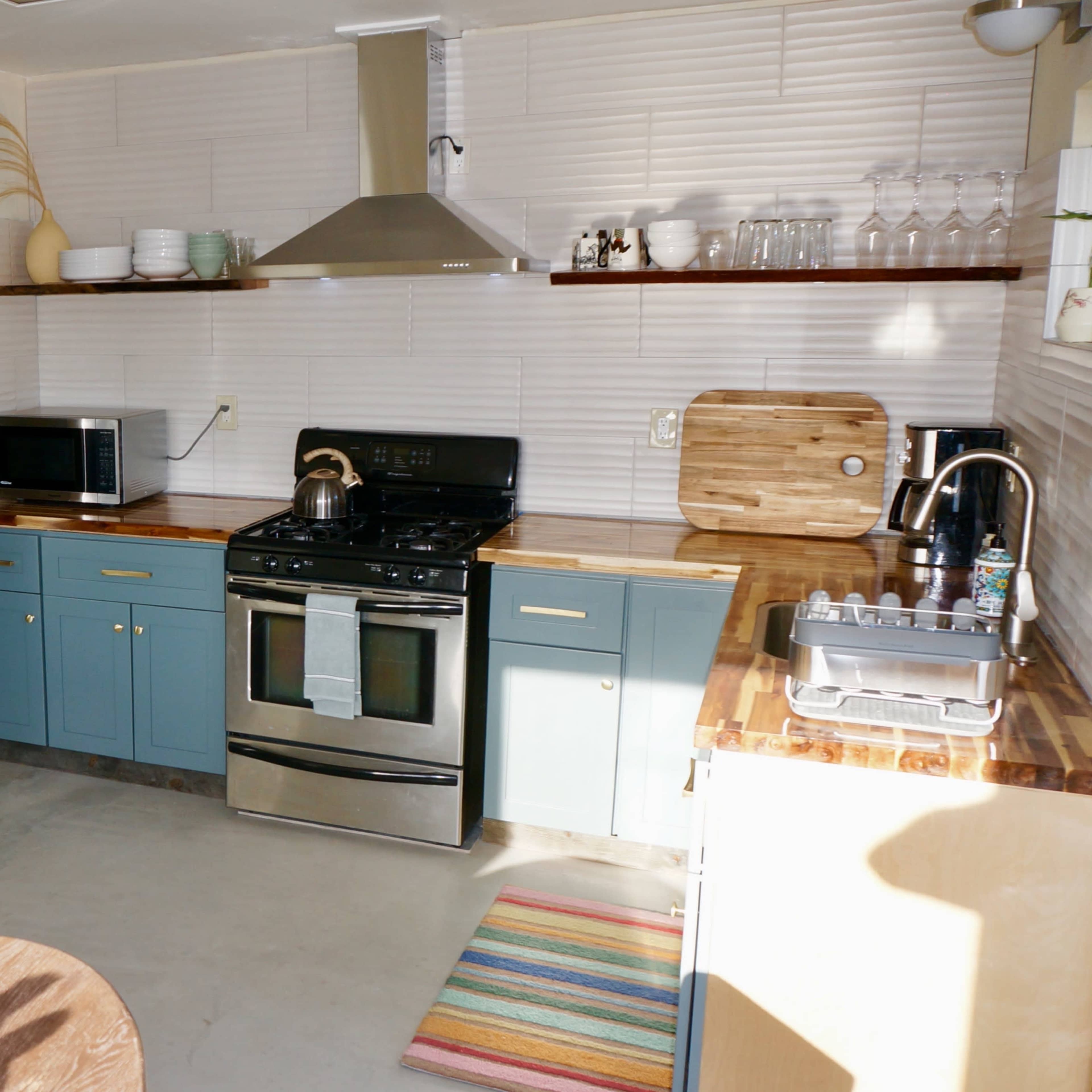 A modern kitchen with stainless steel appliances, blue cabinets, wooden countertops, and a dining table set nearby.