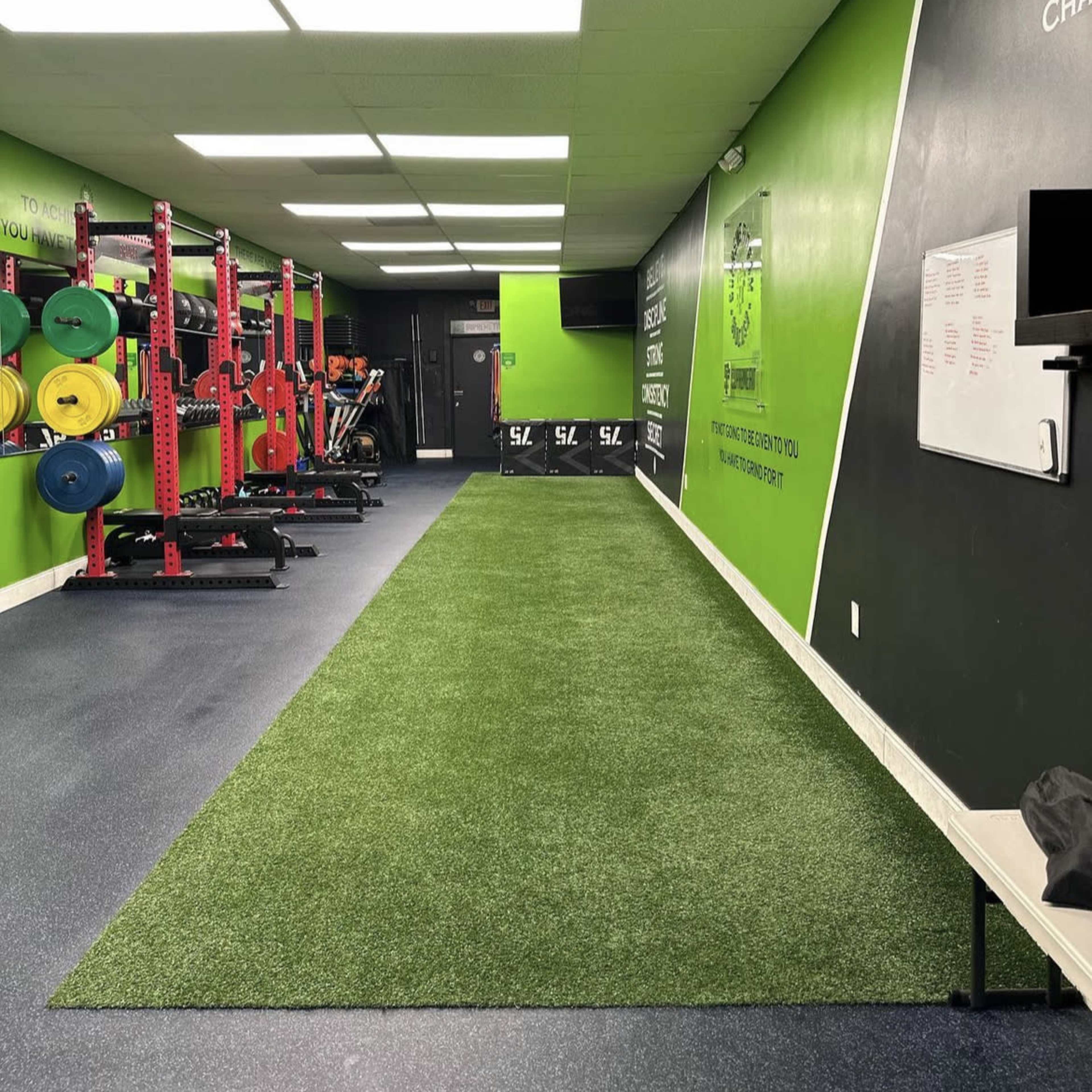 A fitness gym with a green turf area, weightlifting equipment, and a black wall with motivational quotes.