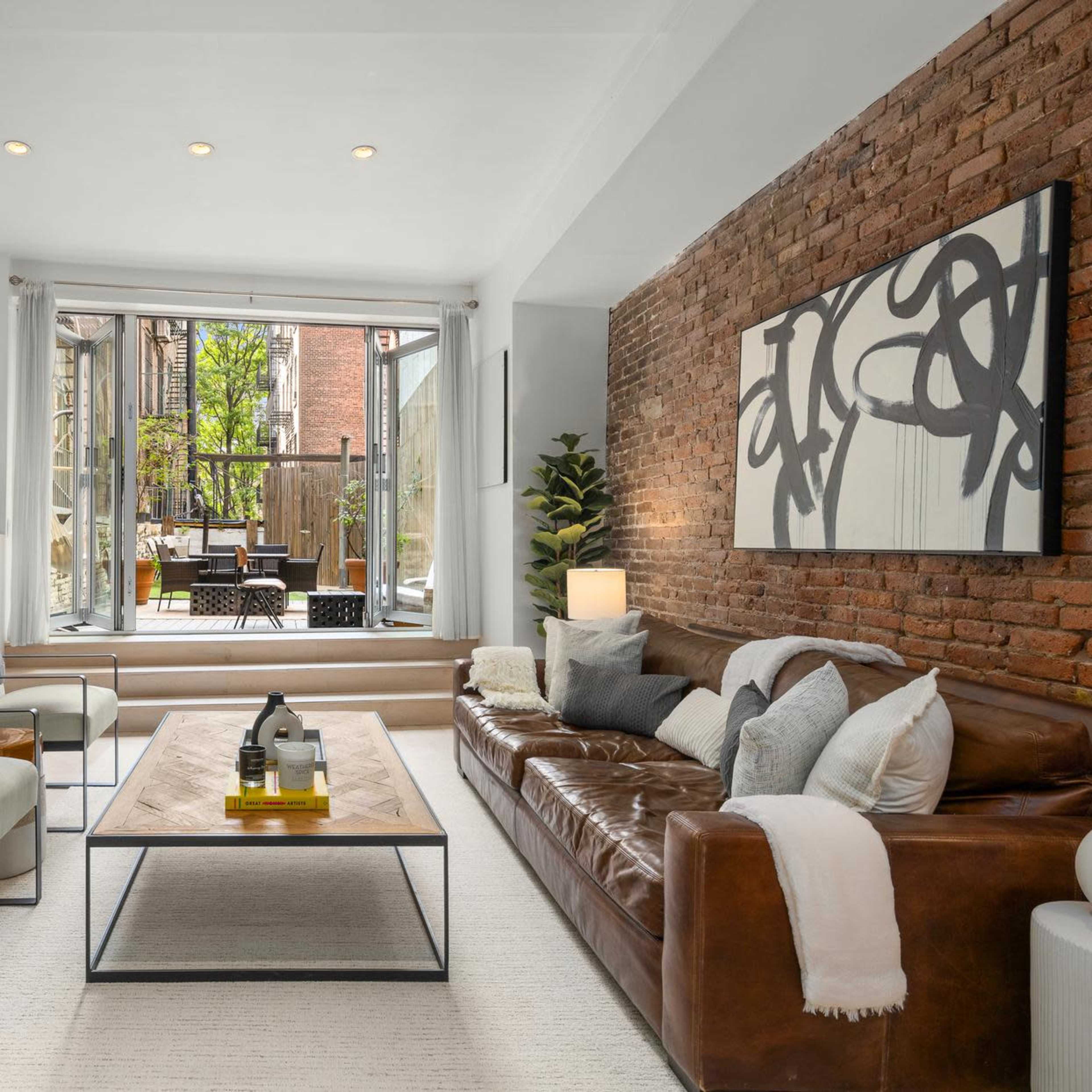 A modern living room with a leather sofa, two chairs, a coffee table, and large windows opening to a patio area.
