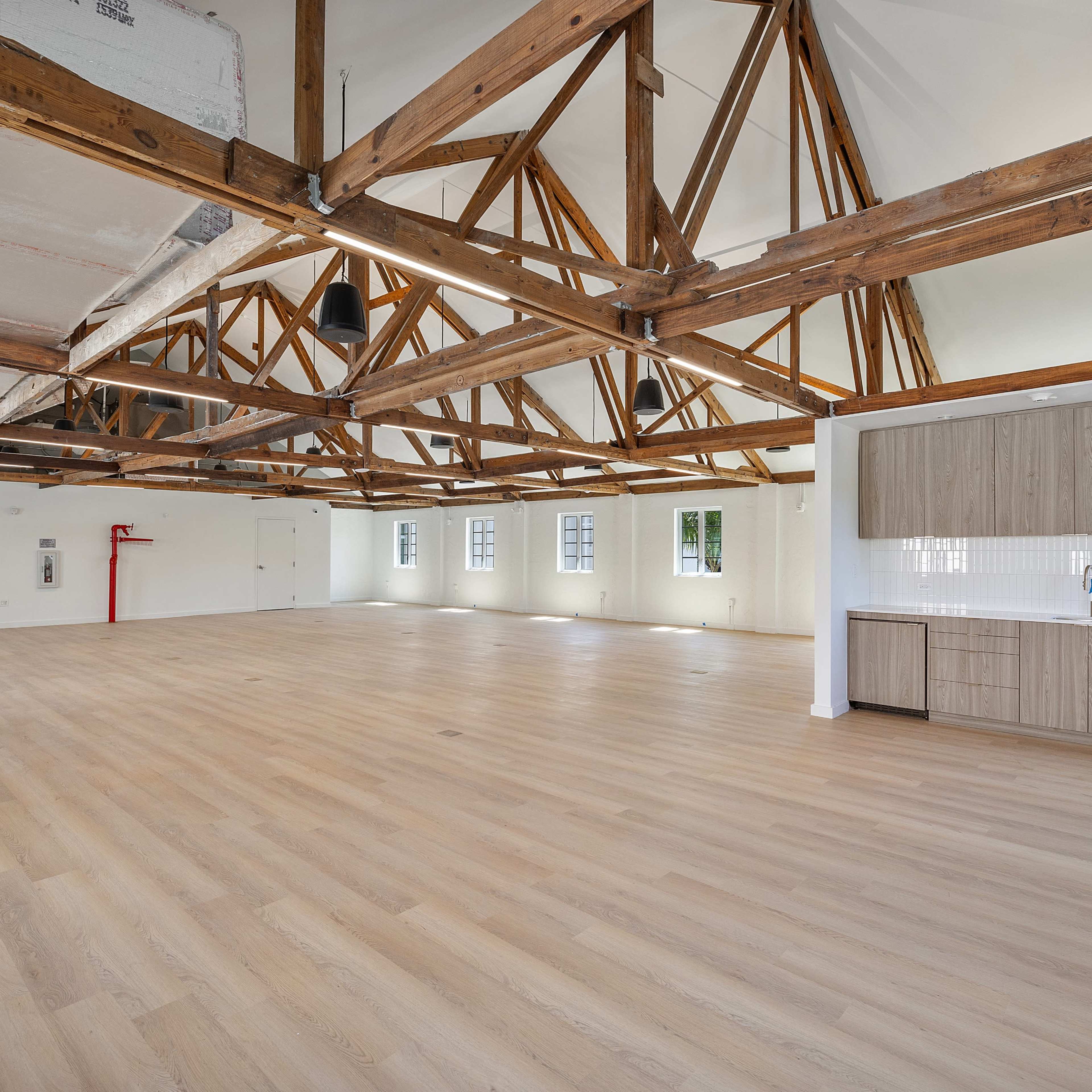 A spacious, empty interior with wooden beams and a kitchenette in one corner.