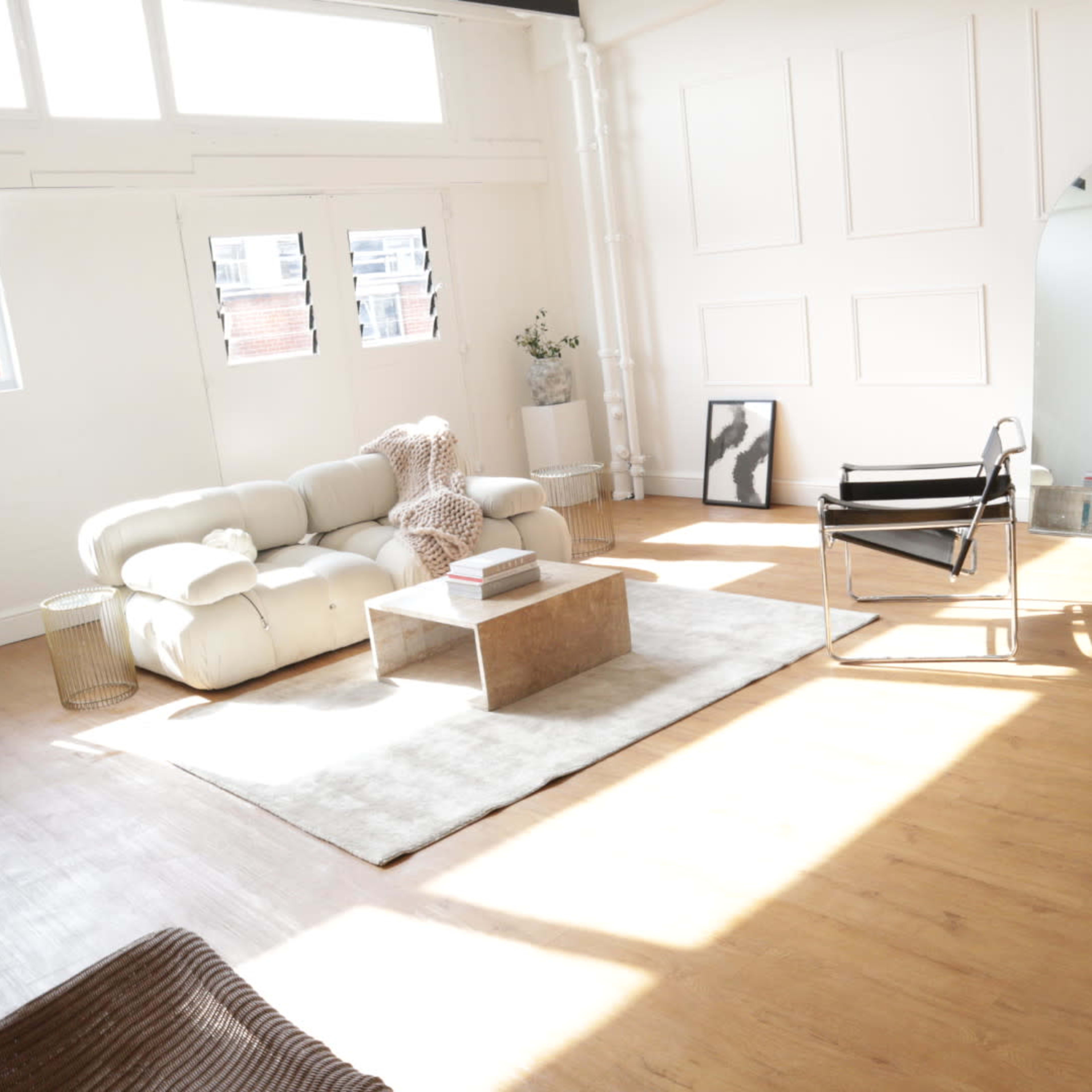 A bright, modern living room with a white sofa, a coffee table, and large windows allowing natural light to fill the space.