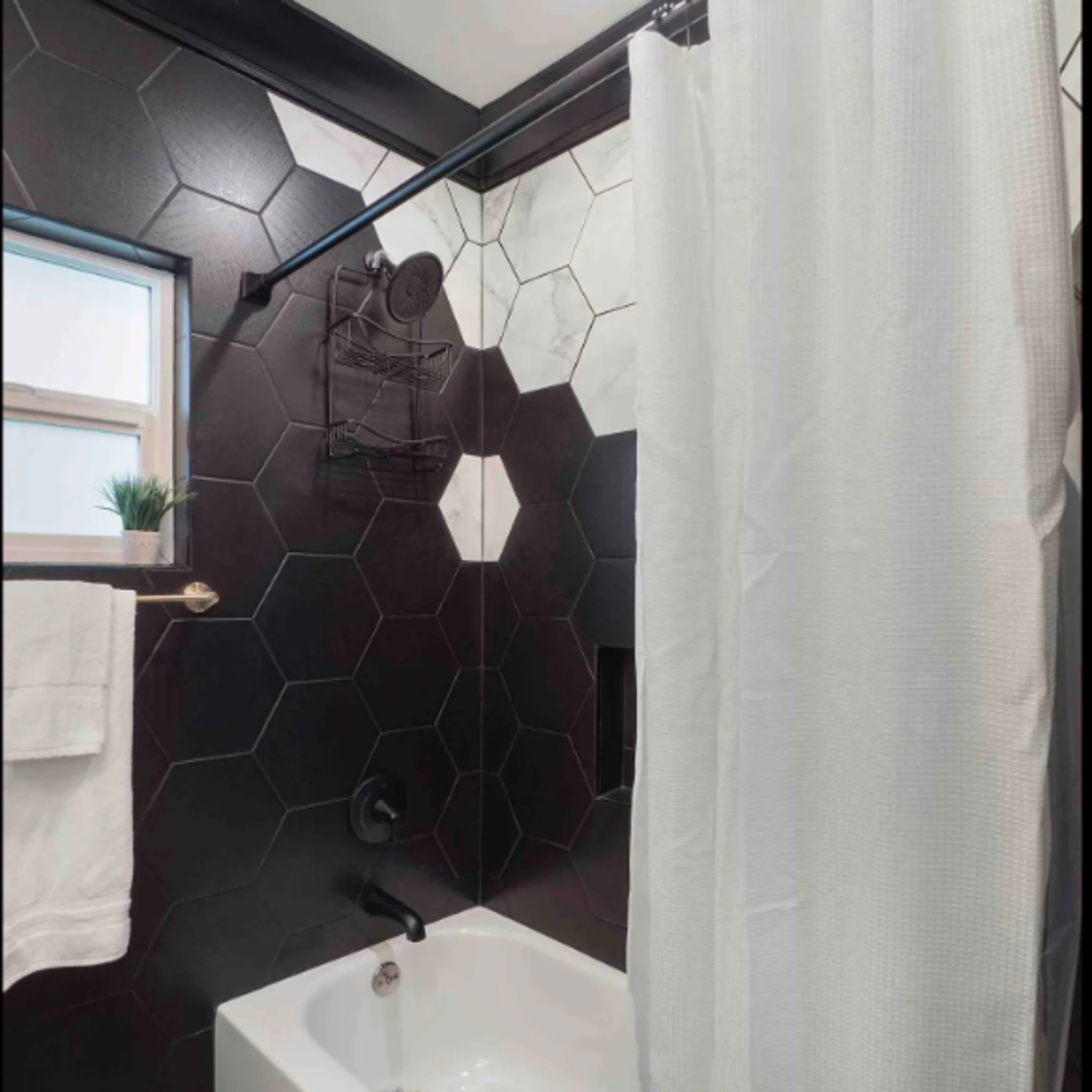A bathroom with a hexagonal tile wall, a white shower curtain, and a bathtub with a dark rug.