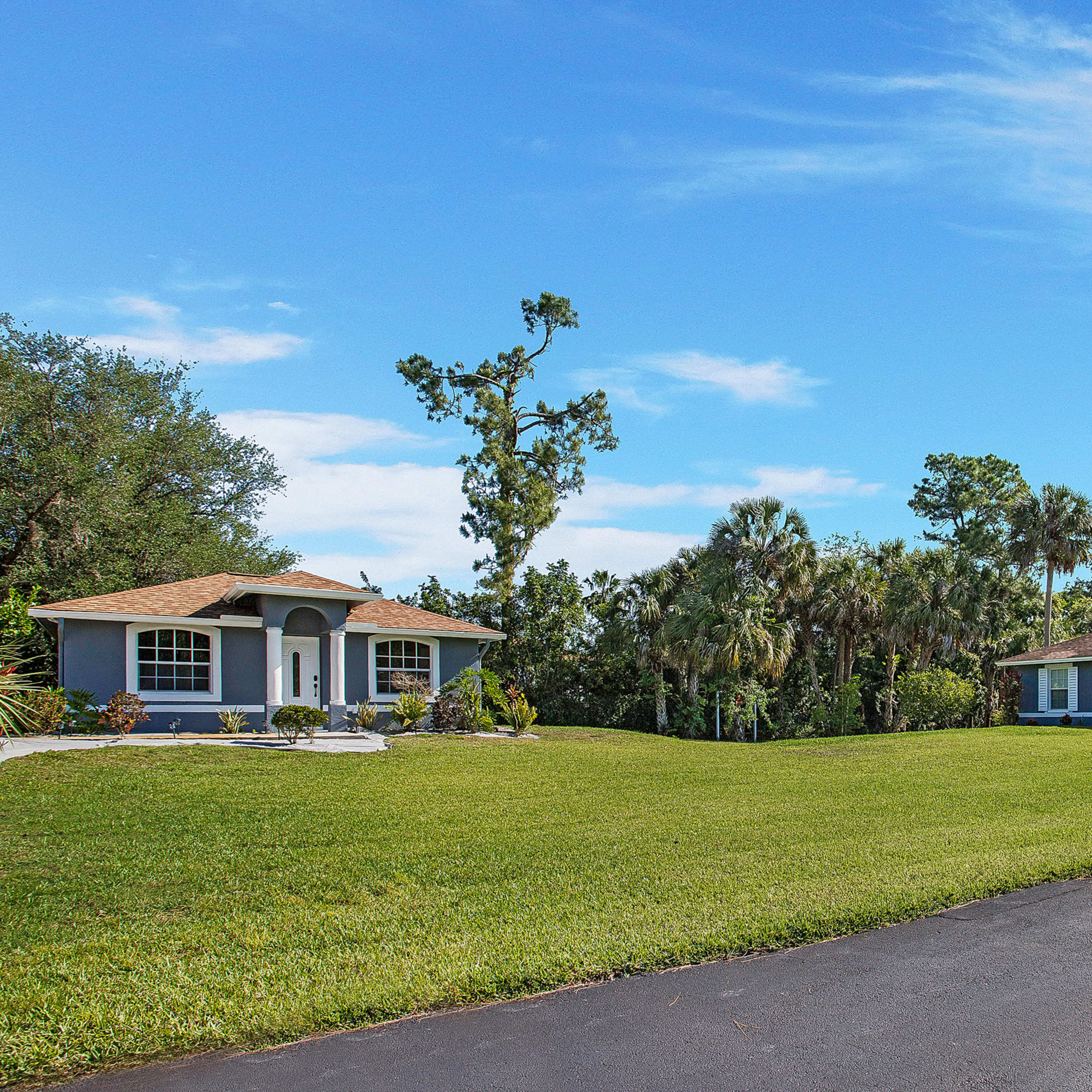 Two residential houses set on a grassy area with trees and palm plants in the background.