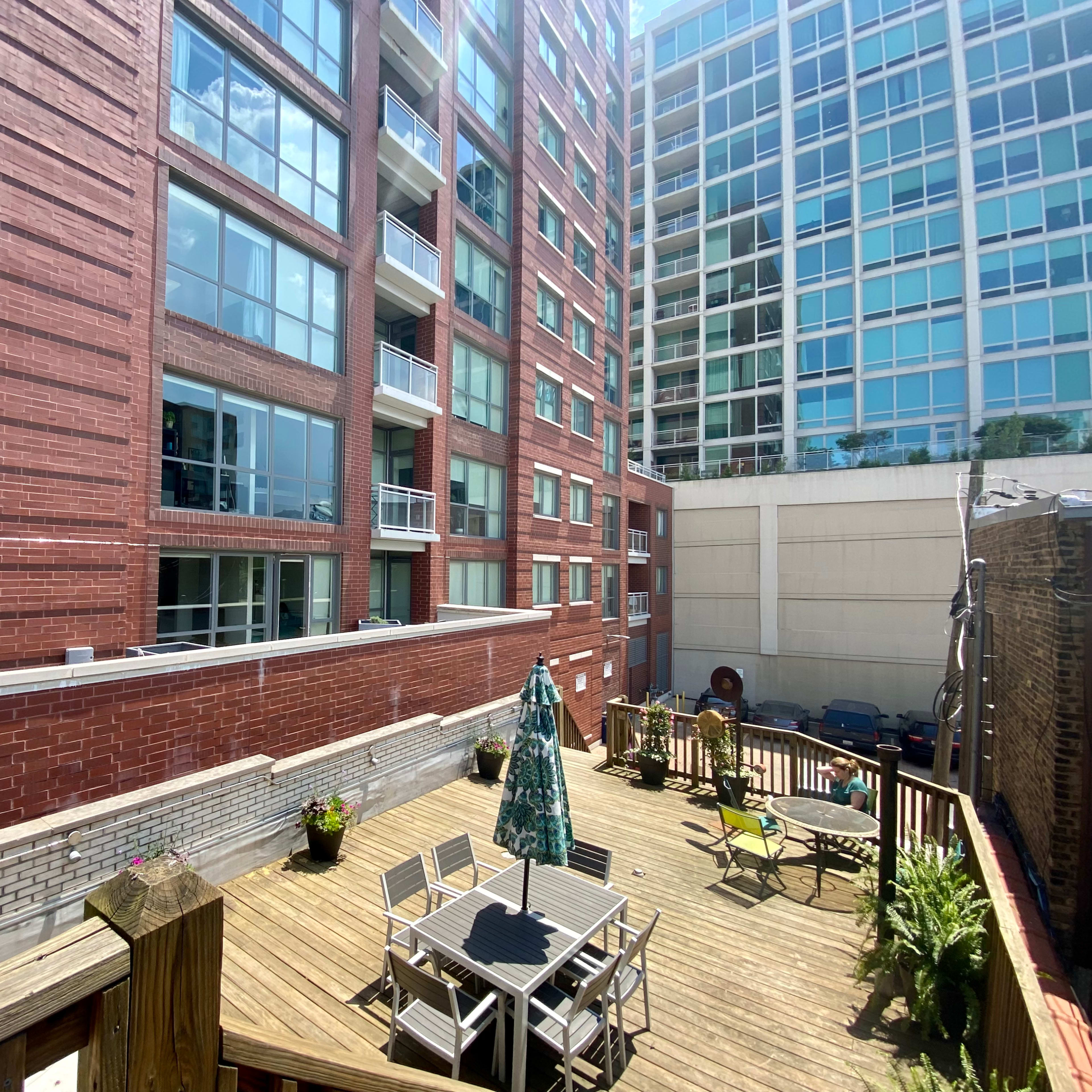 A wooden deck with patio furniture and an umbrella sits between two apartment buildings.