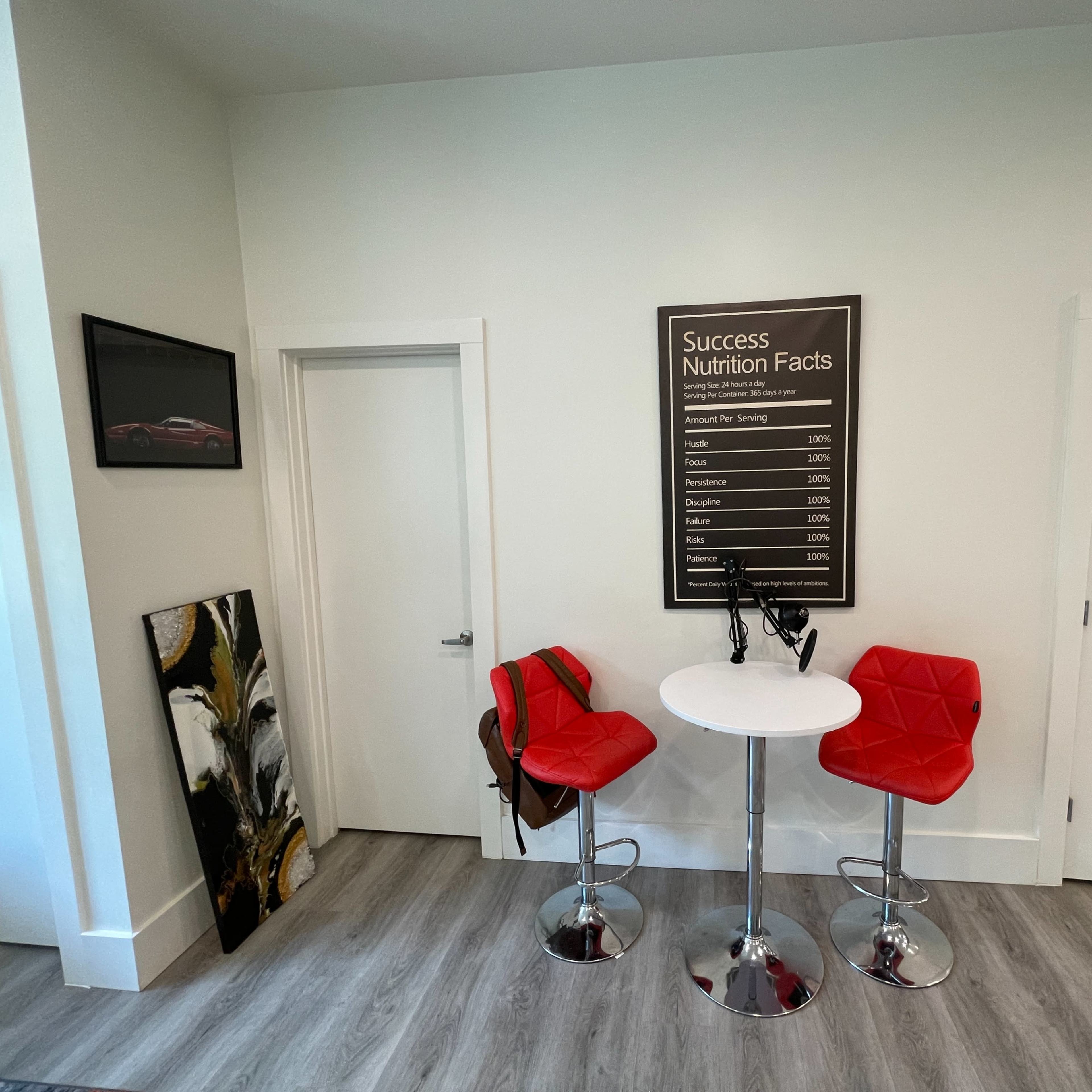 A small interior space with two red bar stools and a round table, featuring a wall-mounted chart labeled "Success Nutrition Facts" and two doors.