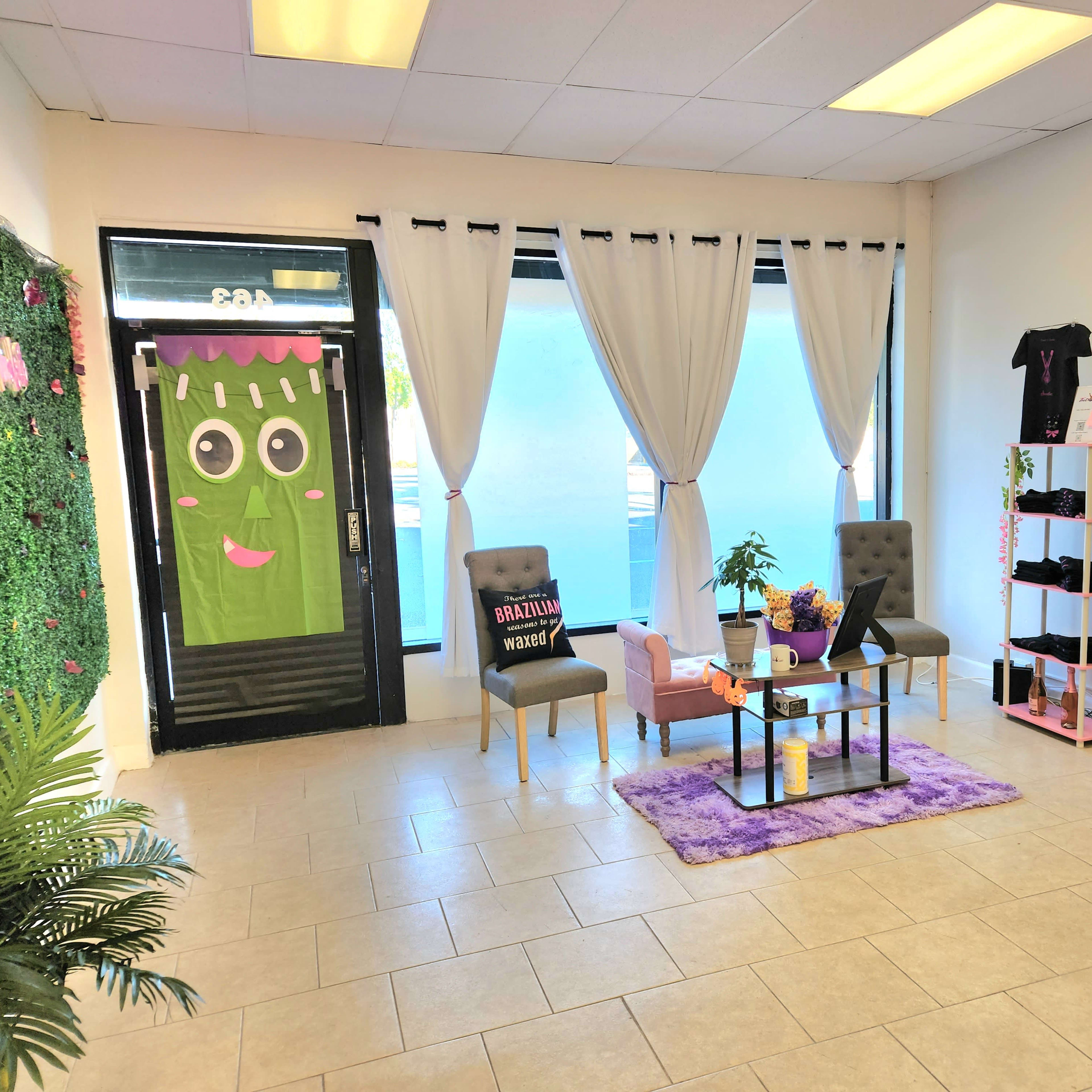 A brightly lit shop interior with two chairs, a table, a small plant, and shelves displaying various products, complemented by decorative elements like curtains and a wall covered in greenery.