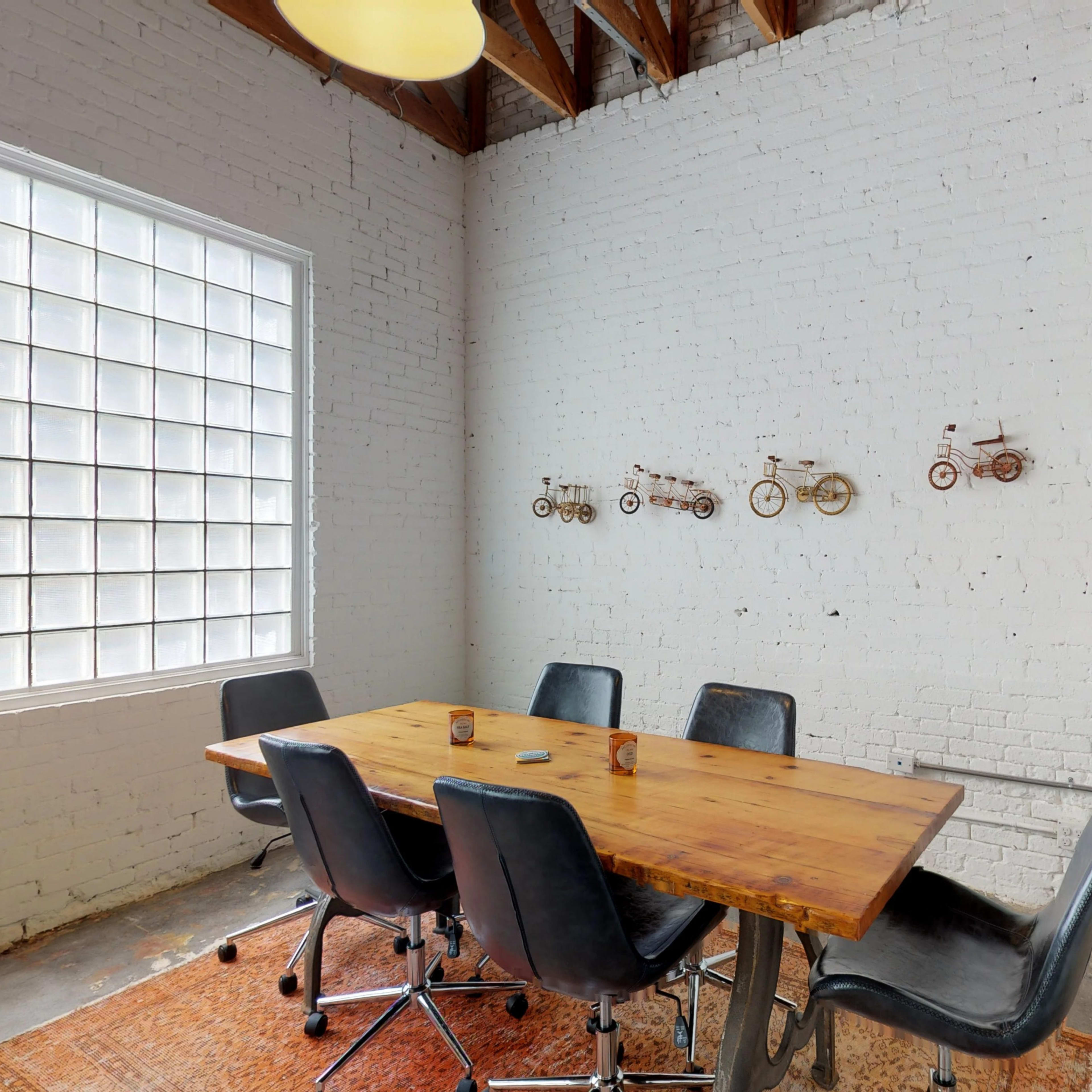A modern conference room features a wooden table surrounded by black chairs, with bicycle-themed decor on the white brick wall.