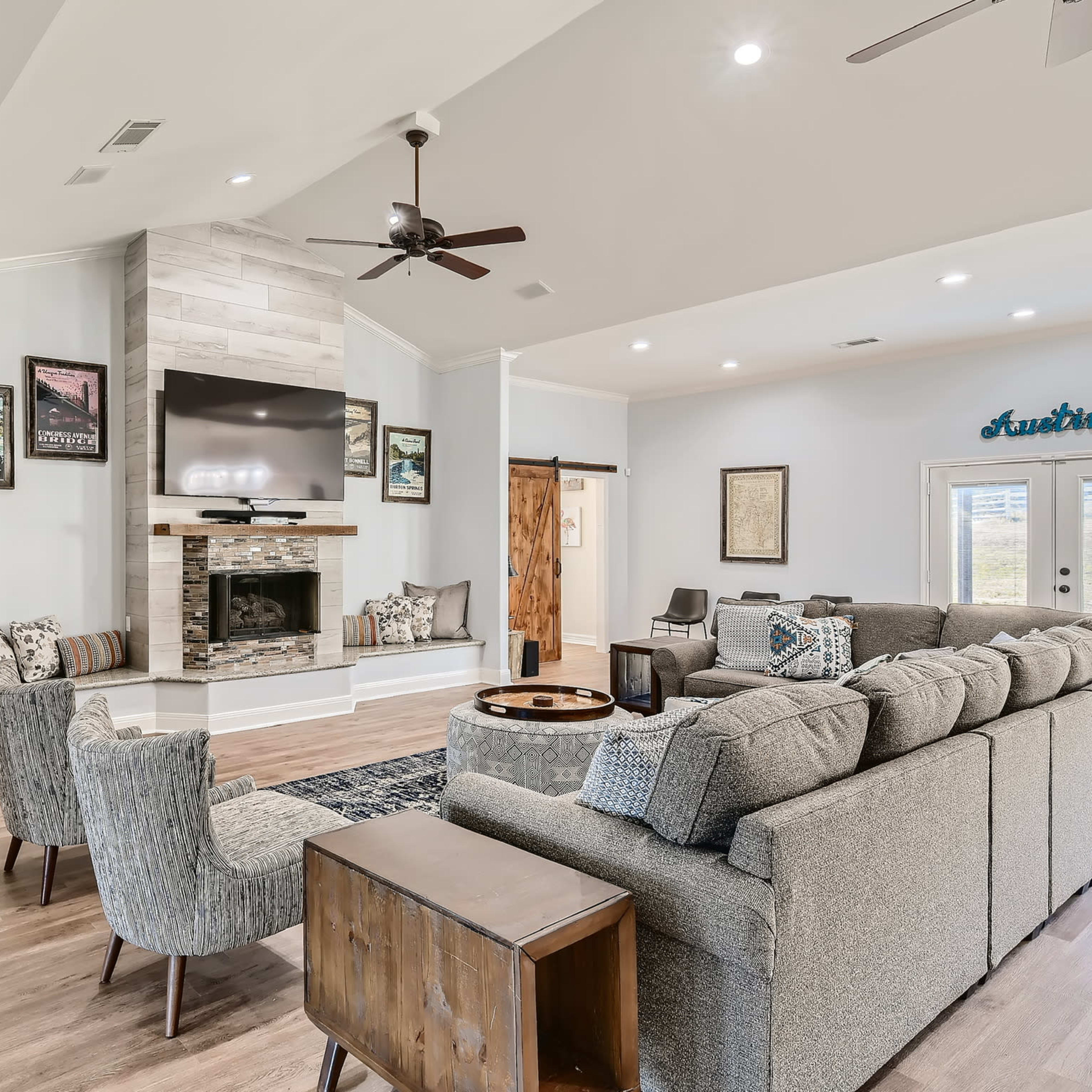 A modern living room featuring a fireplace with a mounted television, comfortable seating, and large windows allowing natural light.