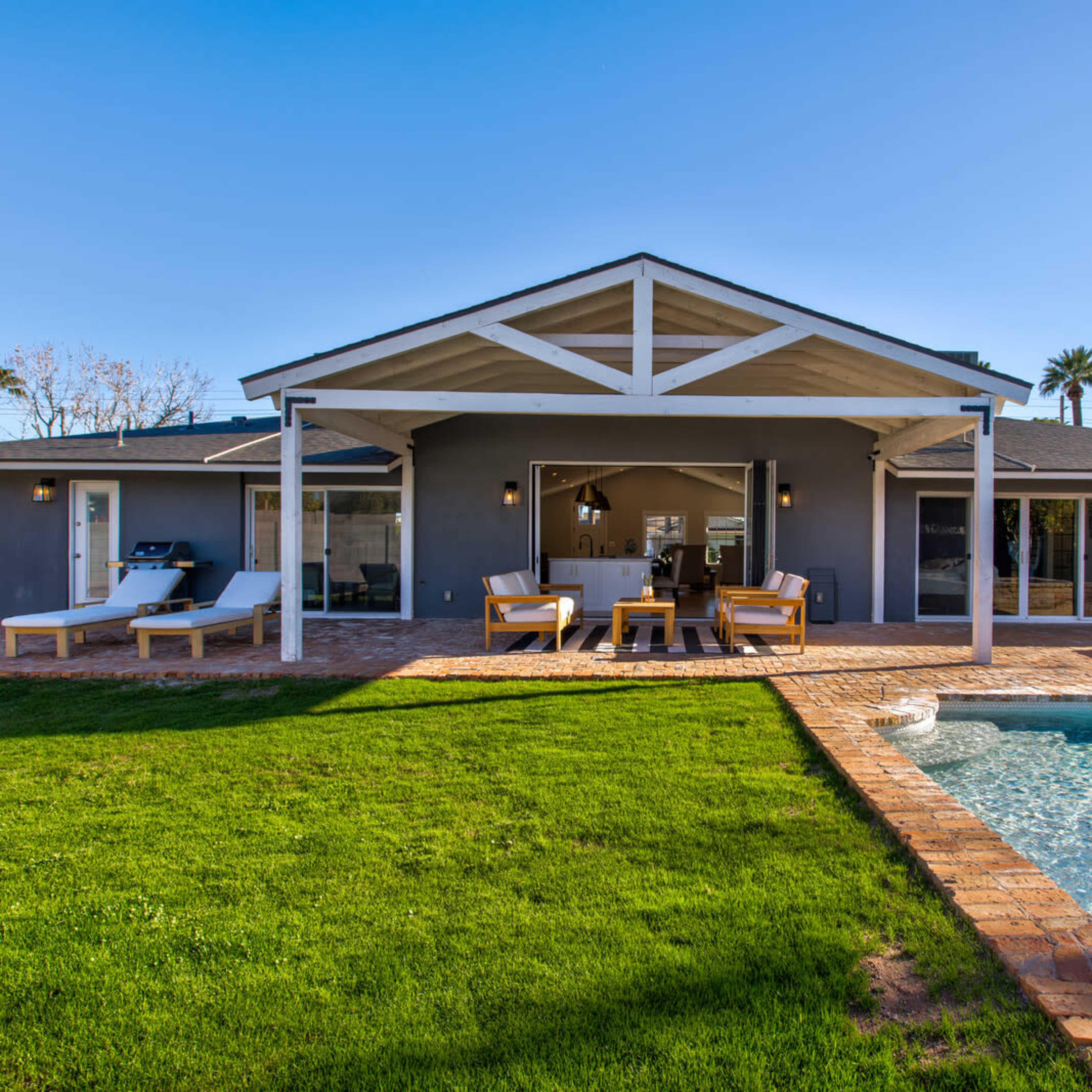 A modern house with a patio and swimming pool is surrounded by a green lawn and palm trees.