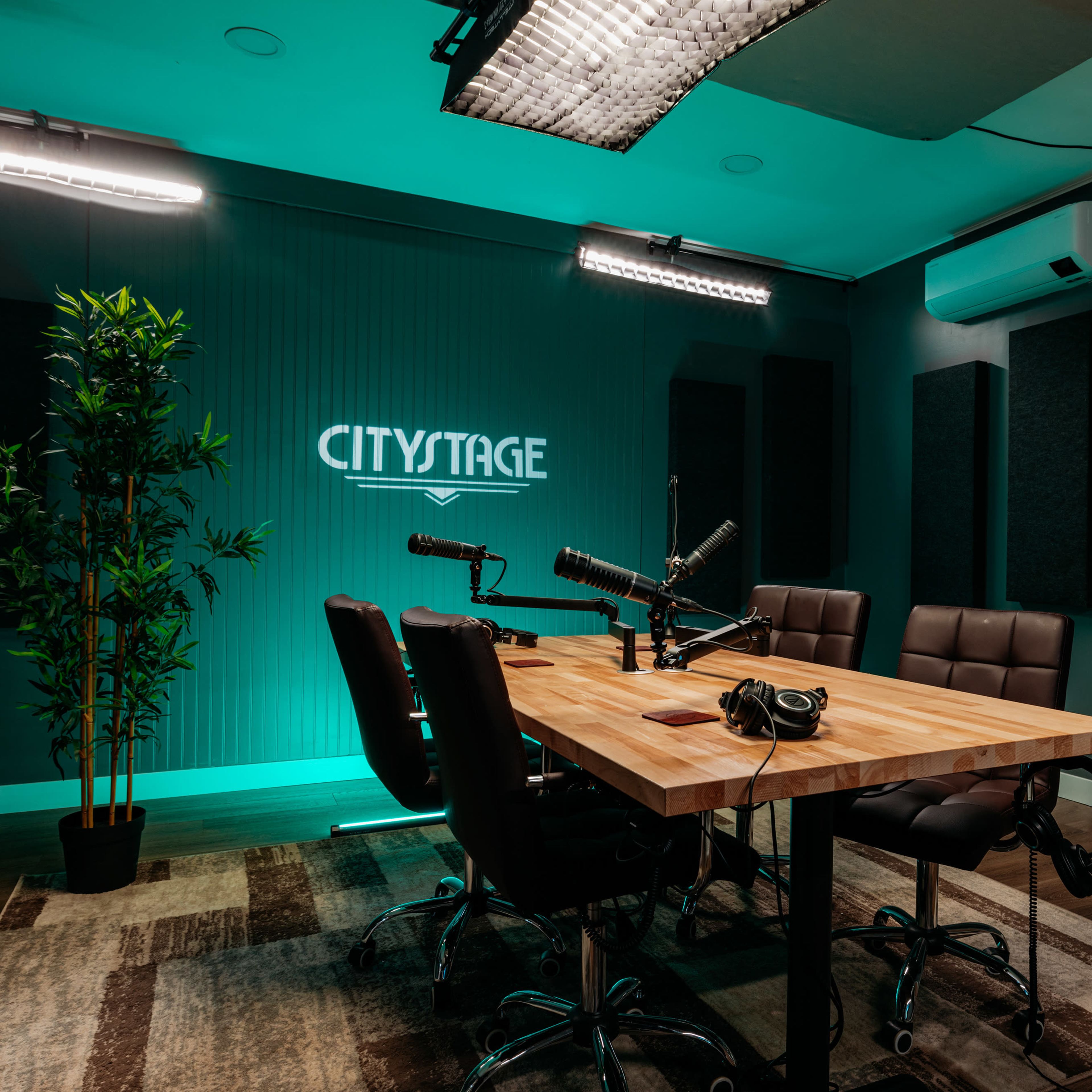 A podcast recording studio features a wooden table surrounded by leather chairs, with microphones and headphones set up, and soundproof panels on the walls.