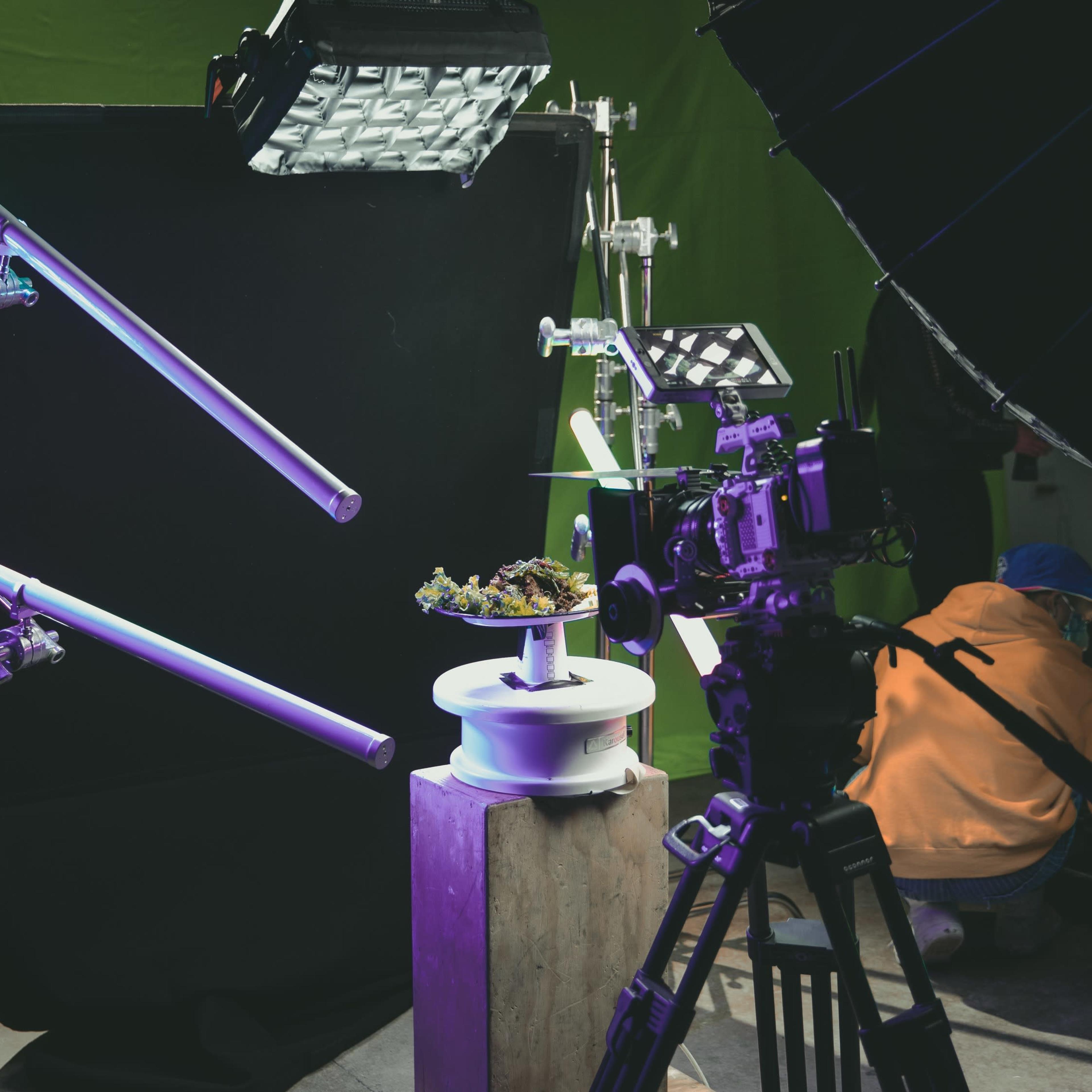 A photography setup with various lighting equipment and a camera directed at a small sculpture on a pedestal, all positioned in front of a green backdrop.