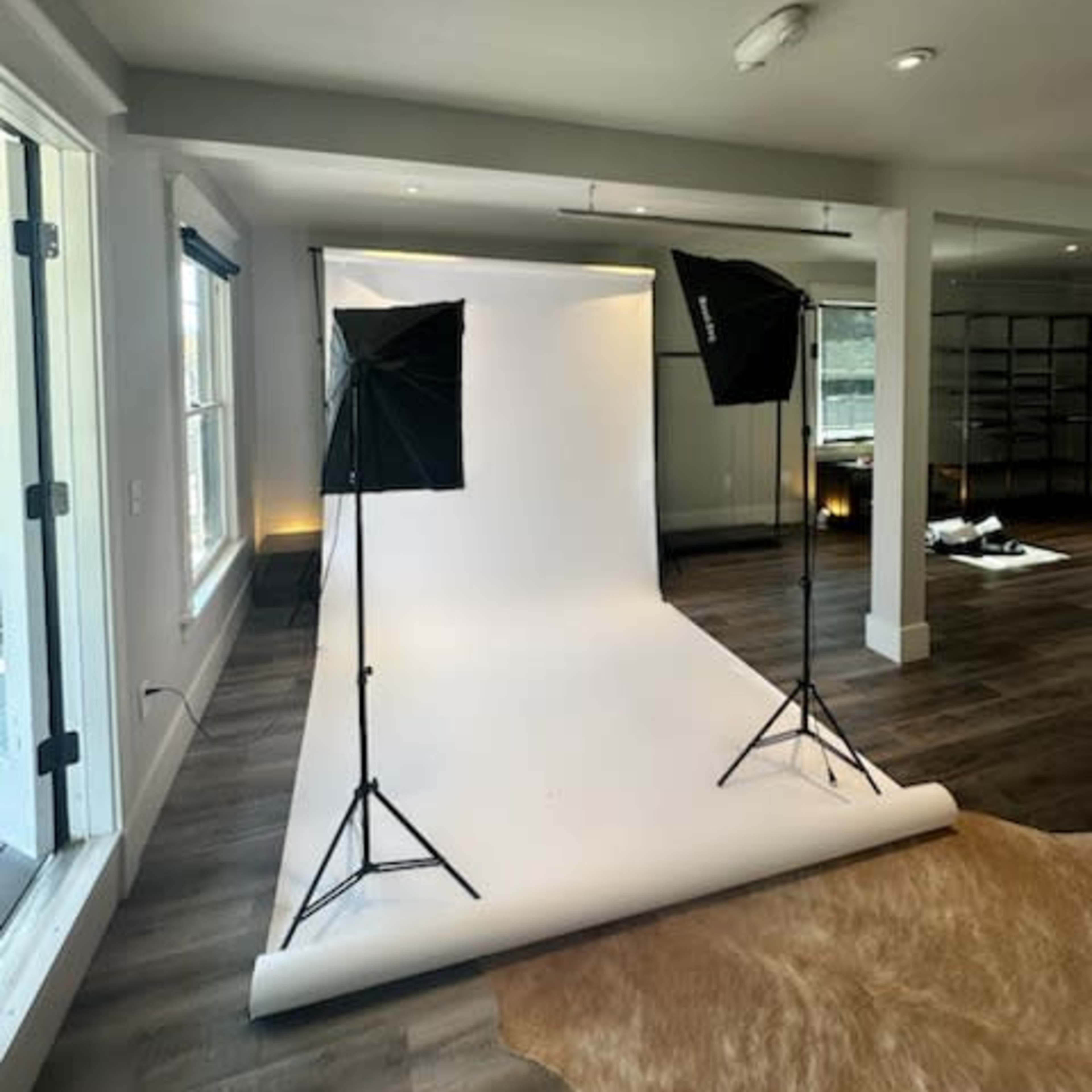 A photography studio setup with a white backdrop and two lighting stands on either side.