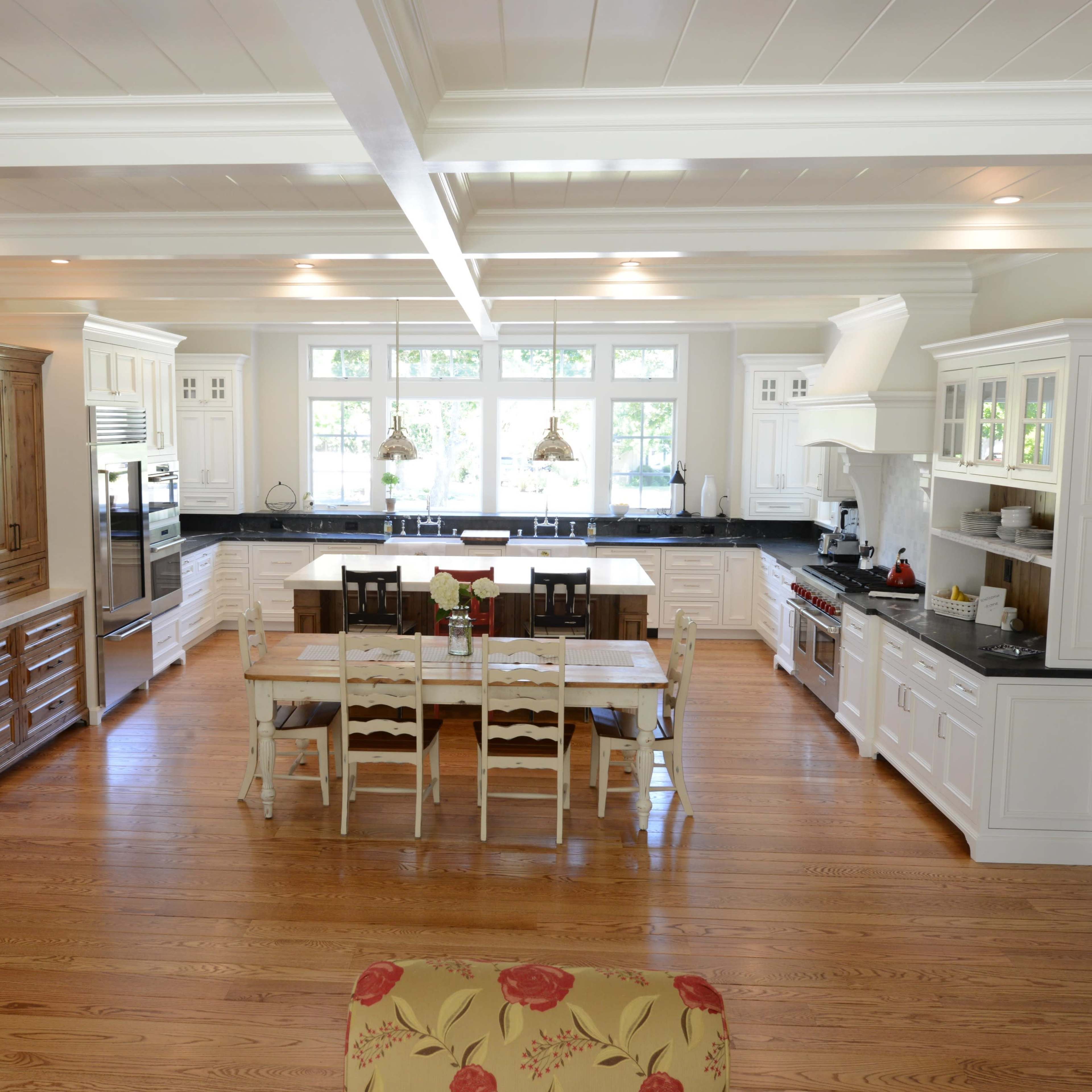 A spacious kitchen with white cabinetry, a large wooden island, and a dining table surrounded by chairs, all set on hardwood flooring.