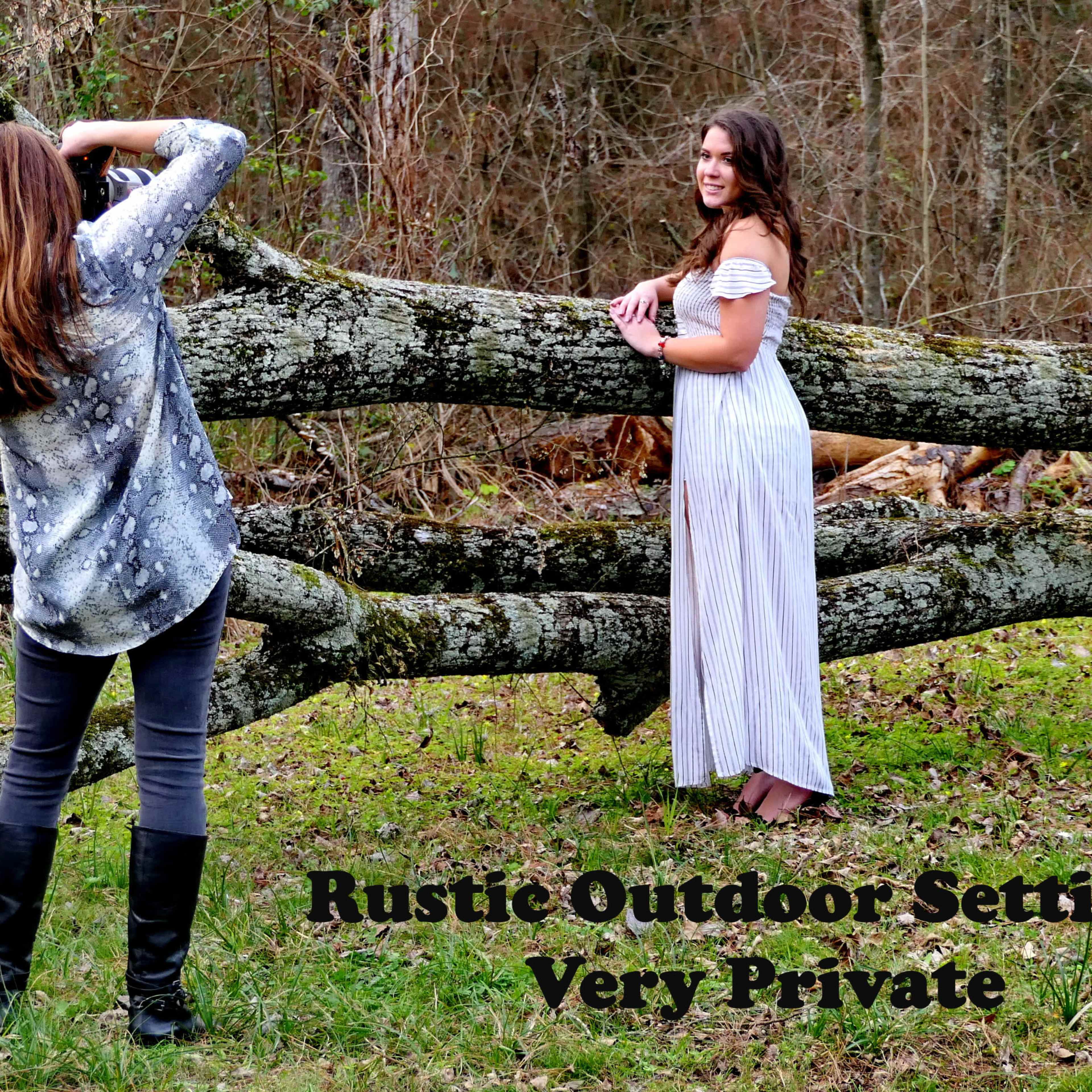 A photographer captures an image of a model posing in a white dress near a fallen log in a wooded area.