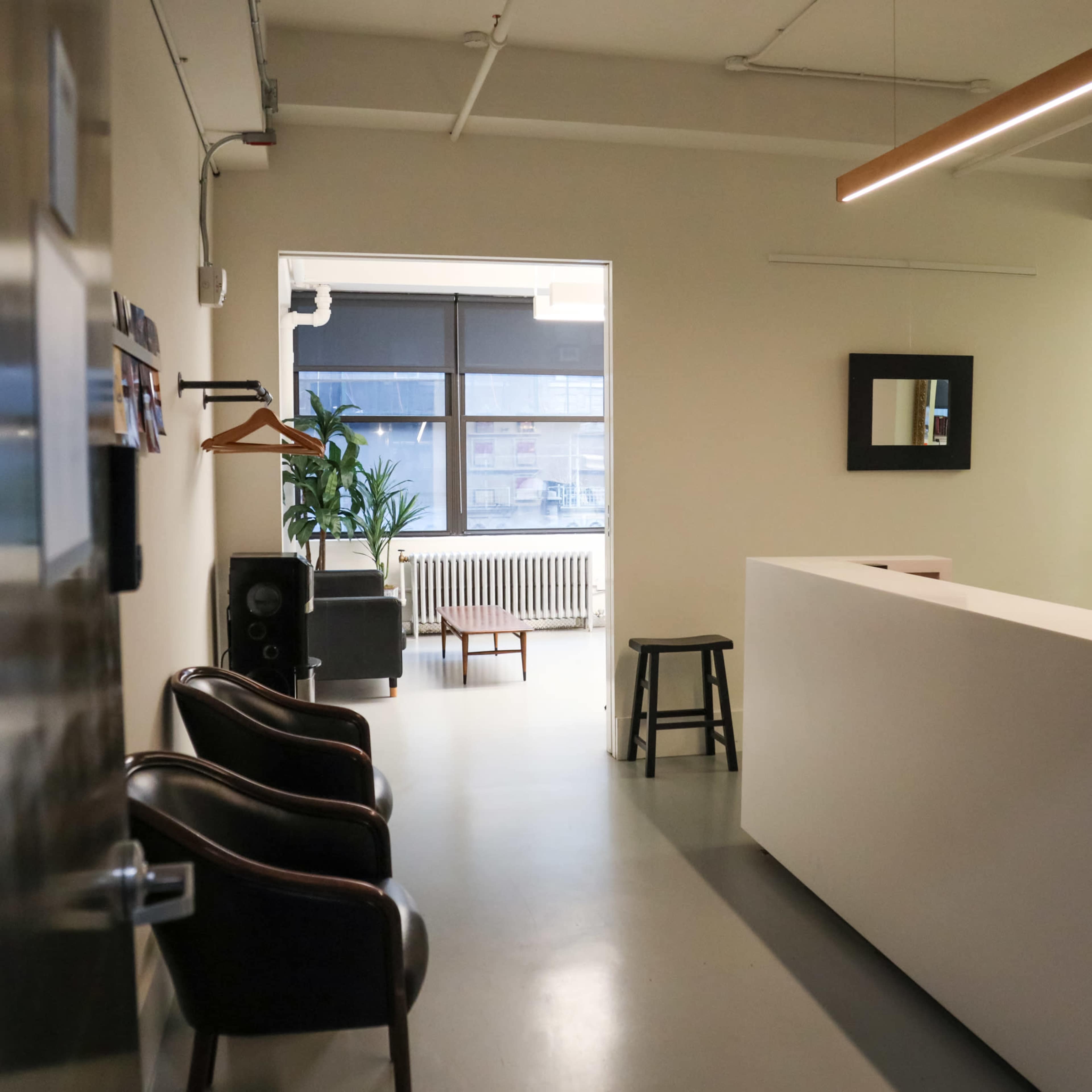 A modern, minimalistic reception area with a white desk, two dark chairs, and a large window providing natural light.