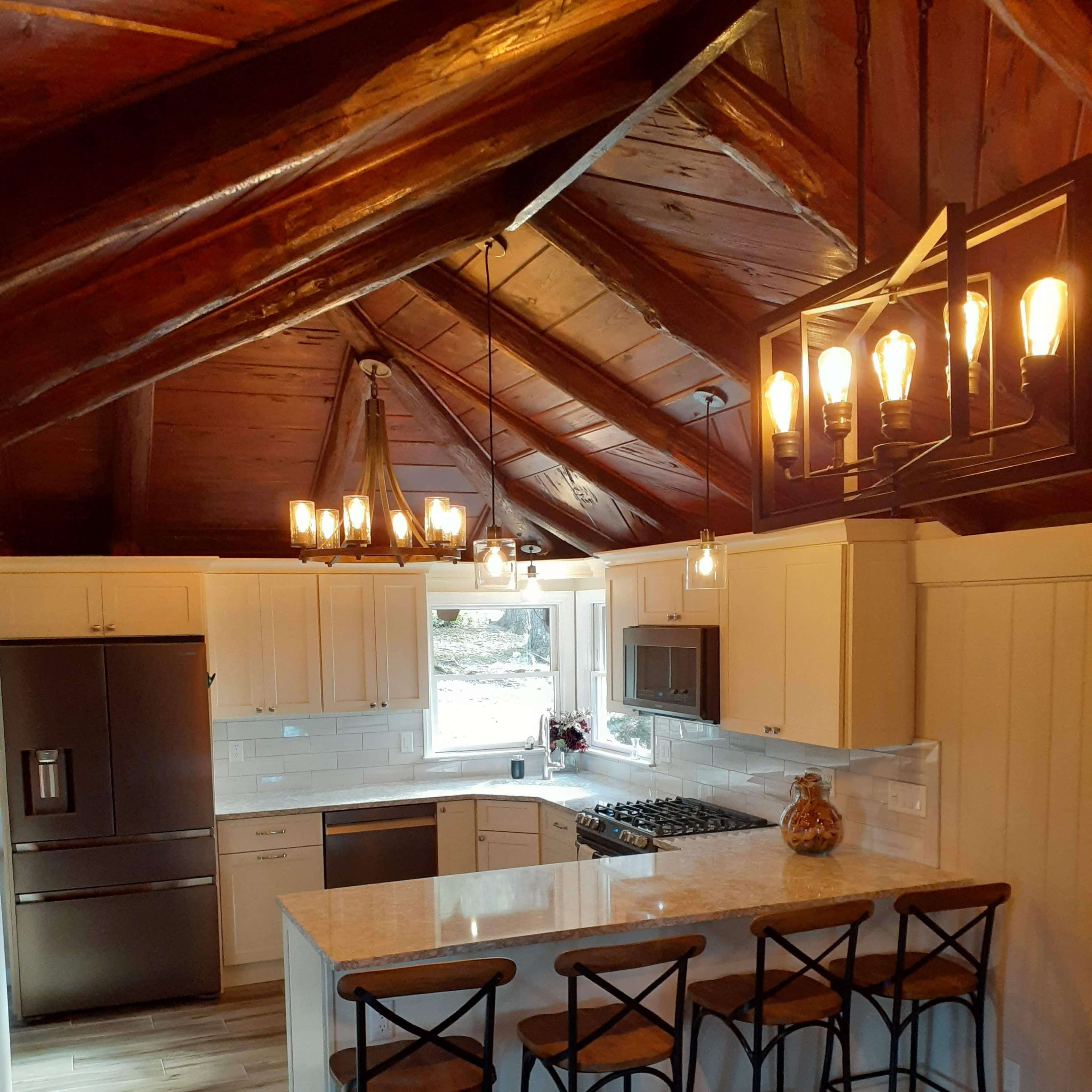A modern kitchen features a large island with bar stools, stainless steel appliances, and wooden ceiling beams.