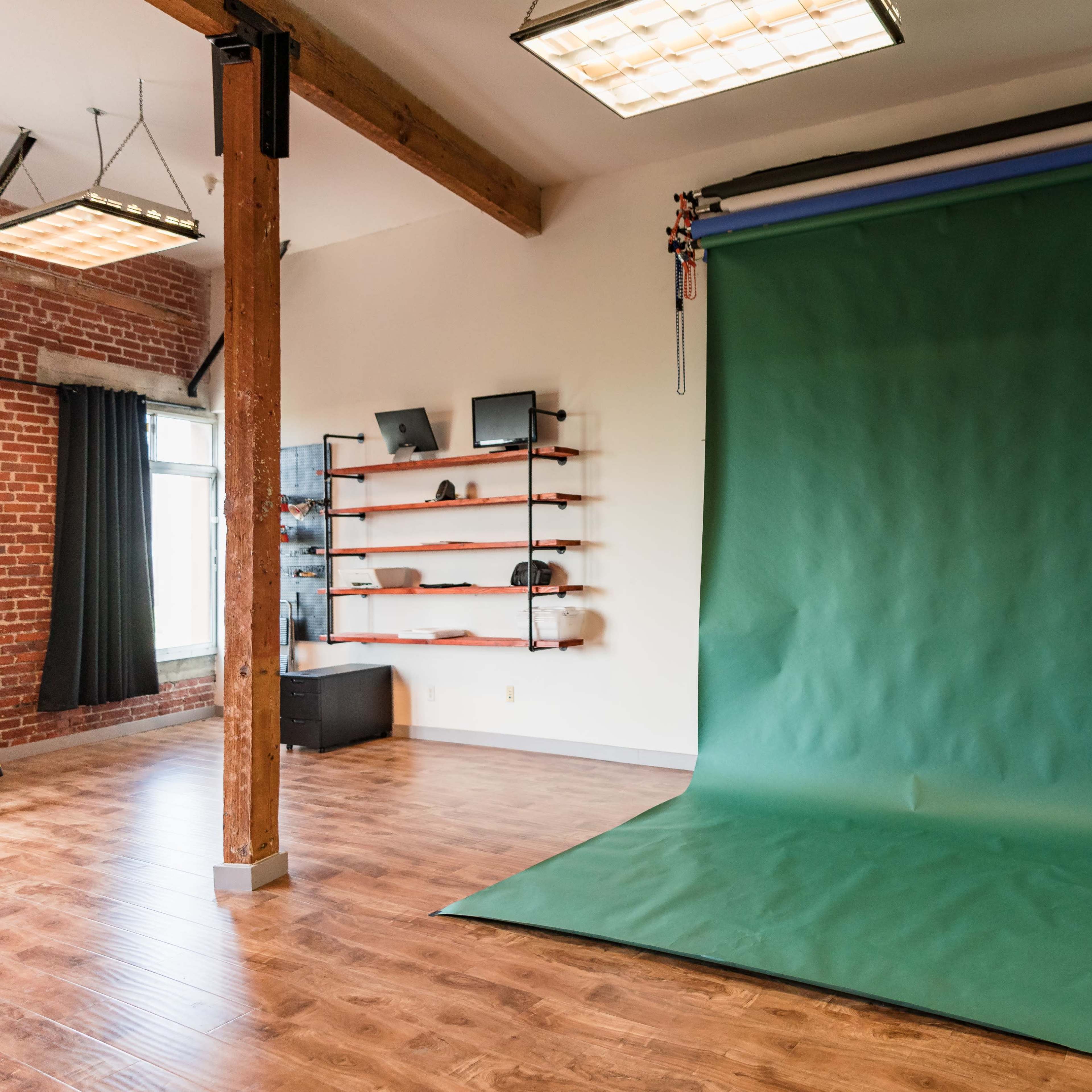 A green backdrop is positioned against a wall in a spacious room with wooden flooring and exposed brick accents.
