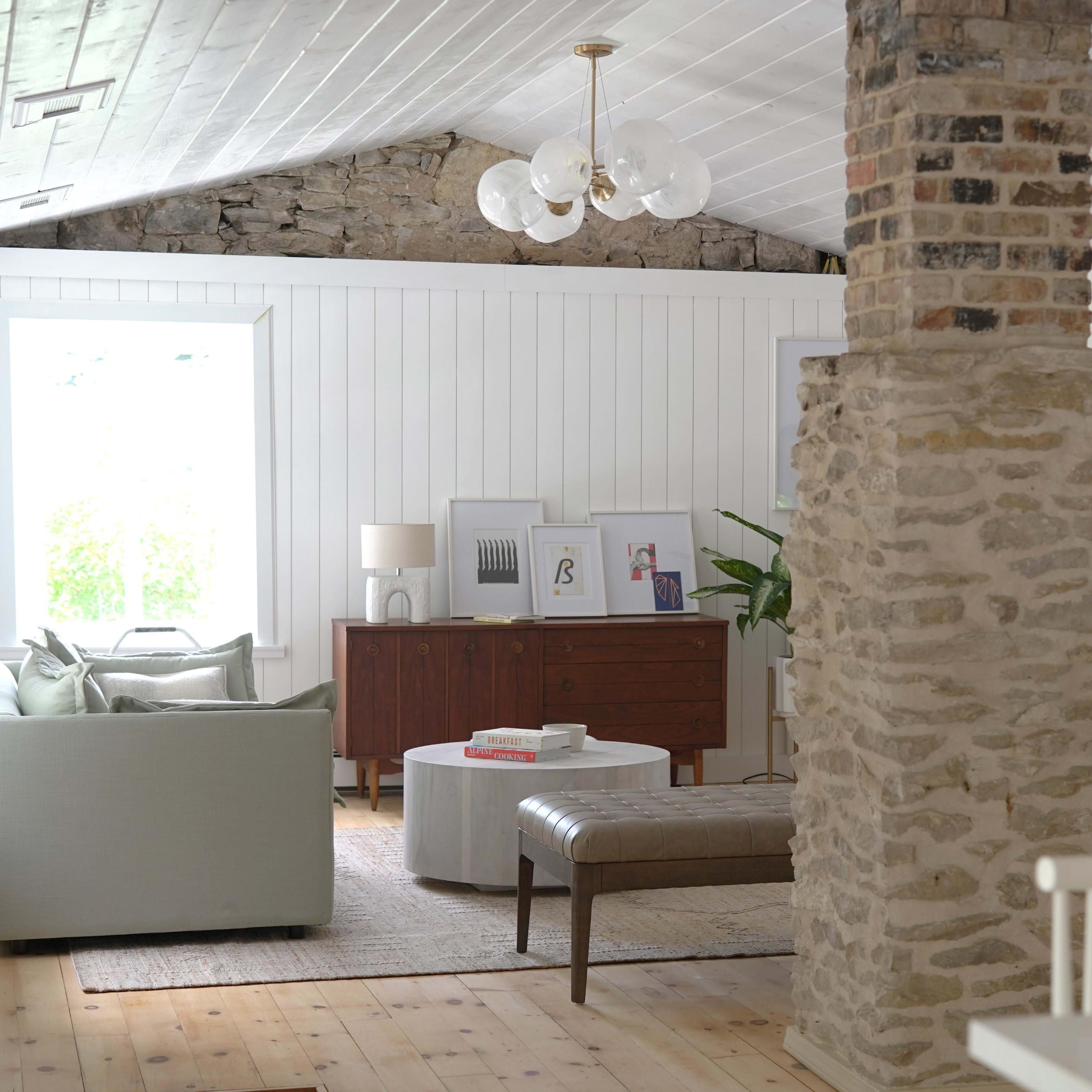 A spacious living room featuring a stone column, a light-colored sofa, a round coffee table, and a mix of modern and vintage furnishings.
