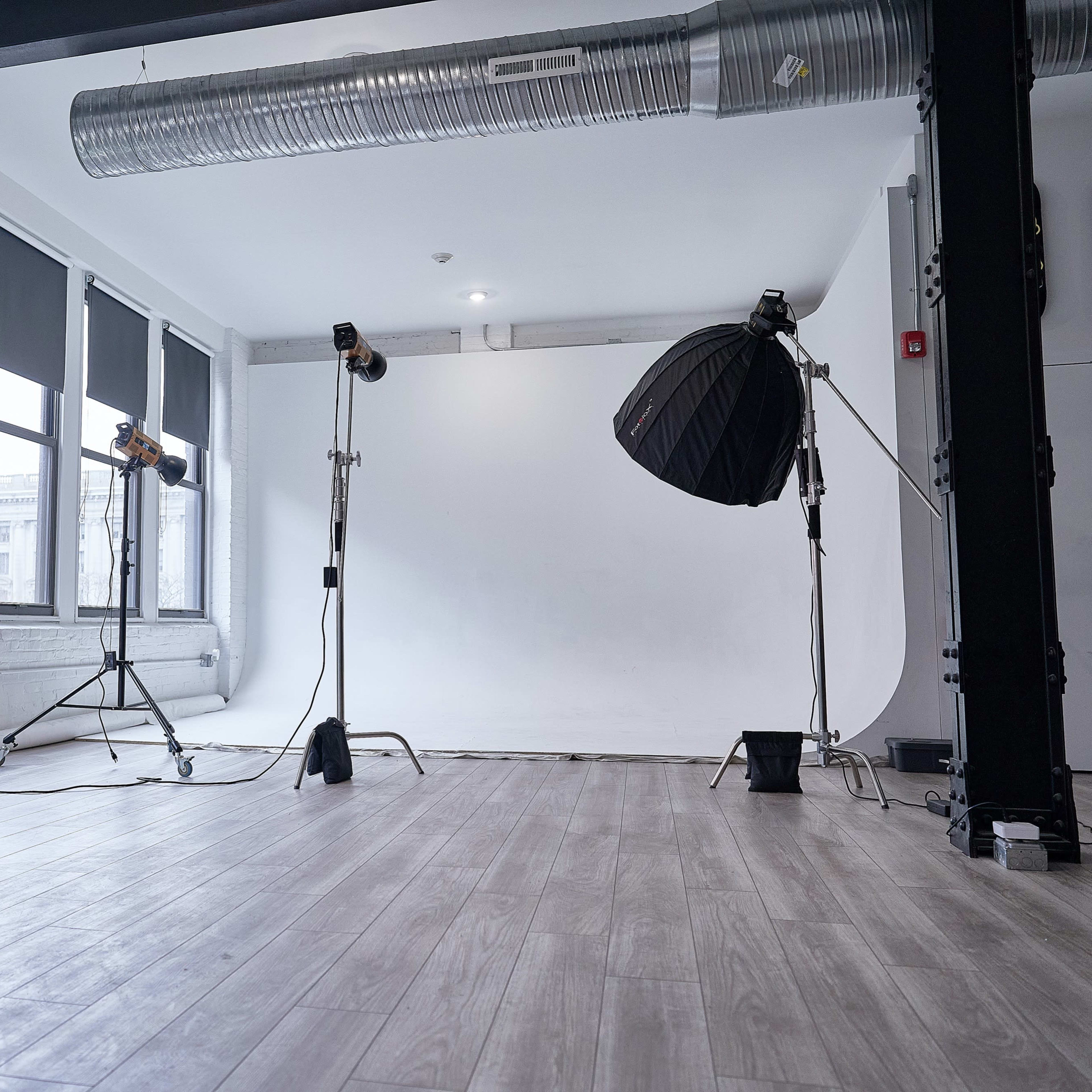 A photo studio with a large white backdrop, studio lights, a mirror, a potted plant, and large windows.