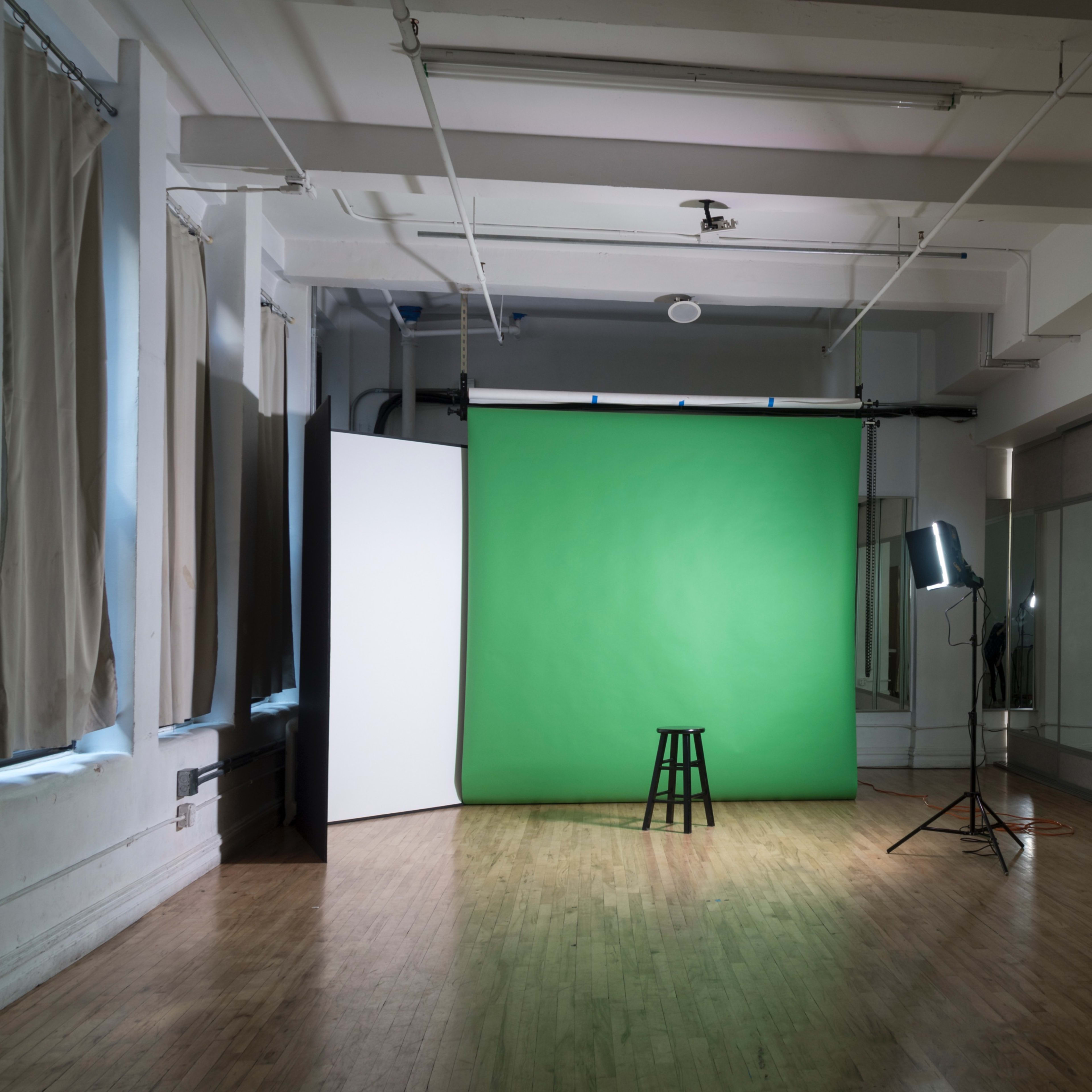 A photography studio features a green backdrop, a wooden stool, lighting equipment, and mirrored walls.