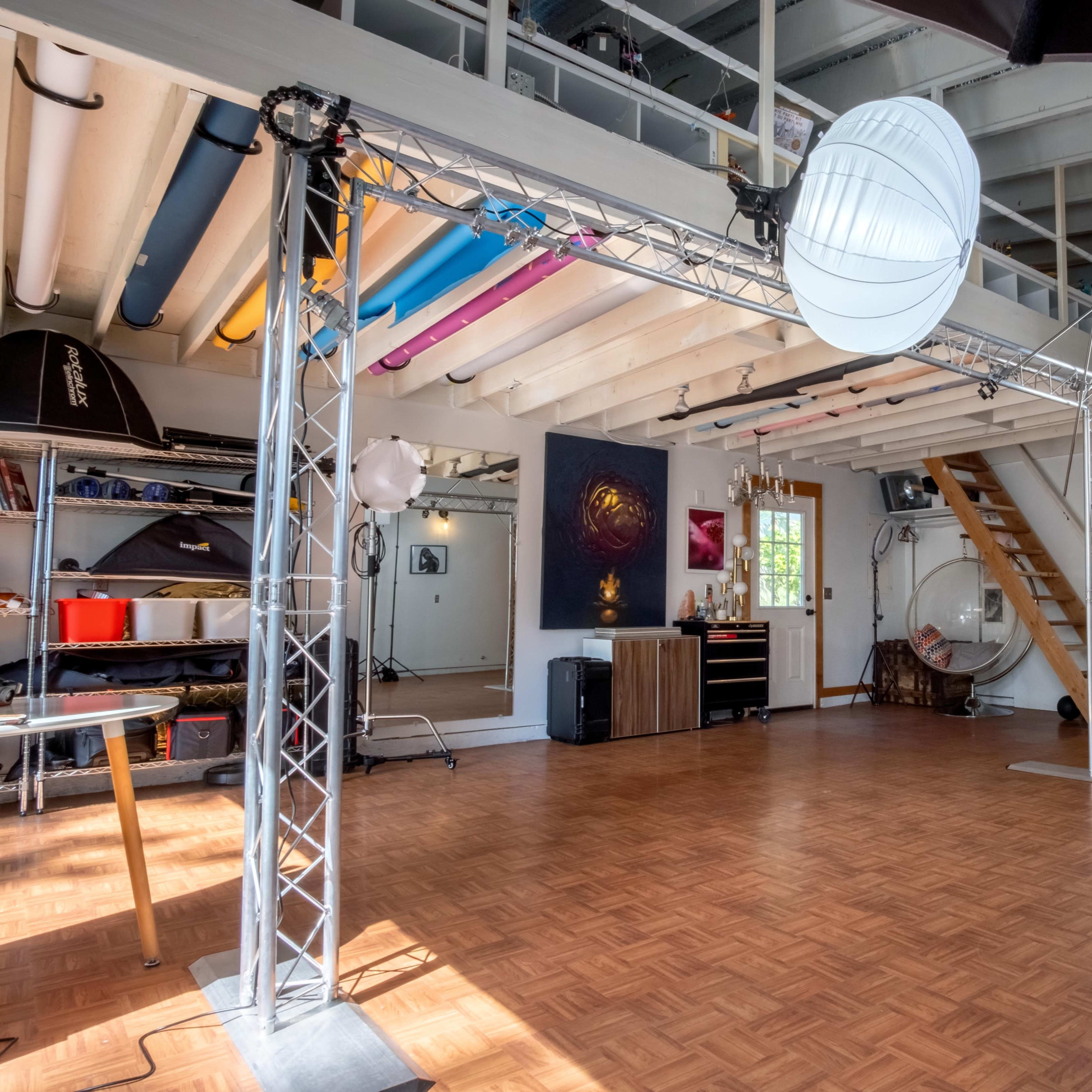 An empty studio space with wooden flooring, soft lighting fixtures, and various equipment along the walls.