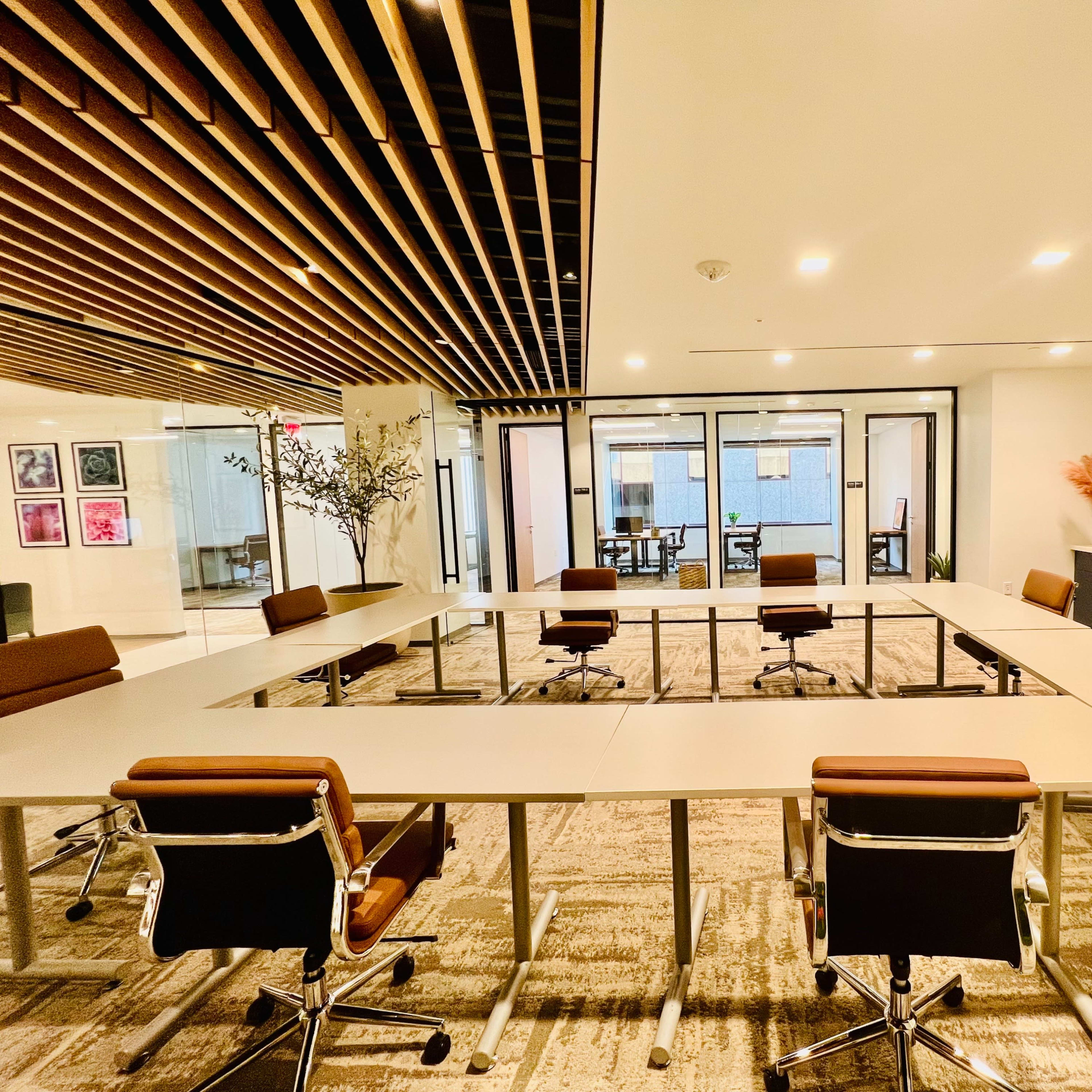 A modern conference room with a large rectangular table surrounded by ergonomic chairs and glass partitions leading to other meeting areas.