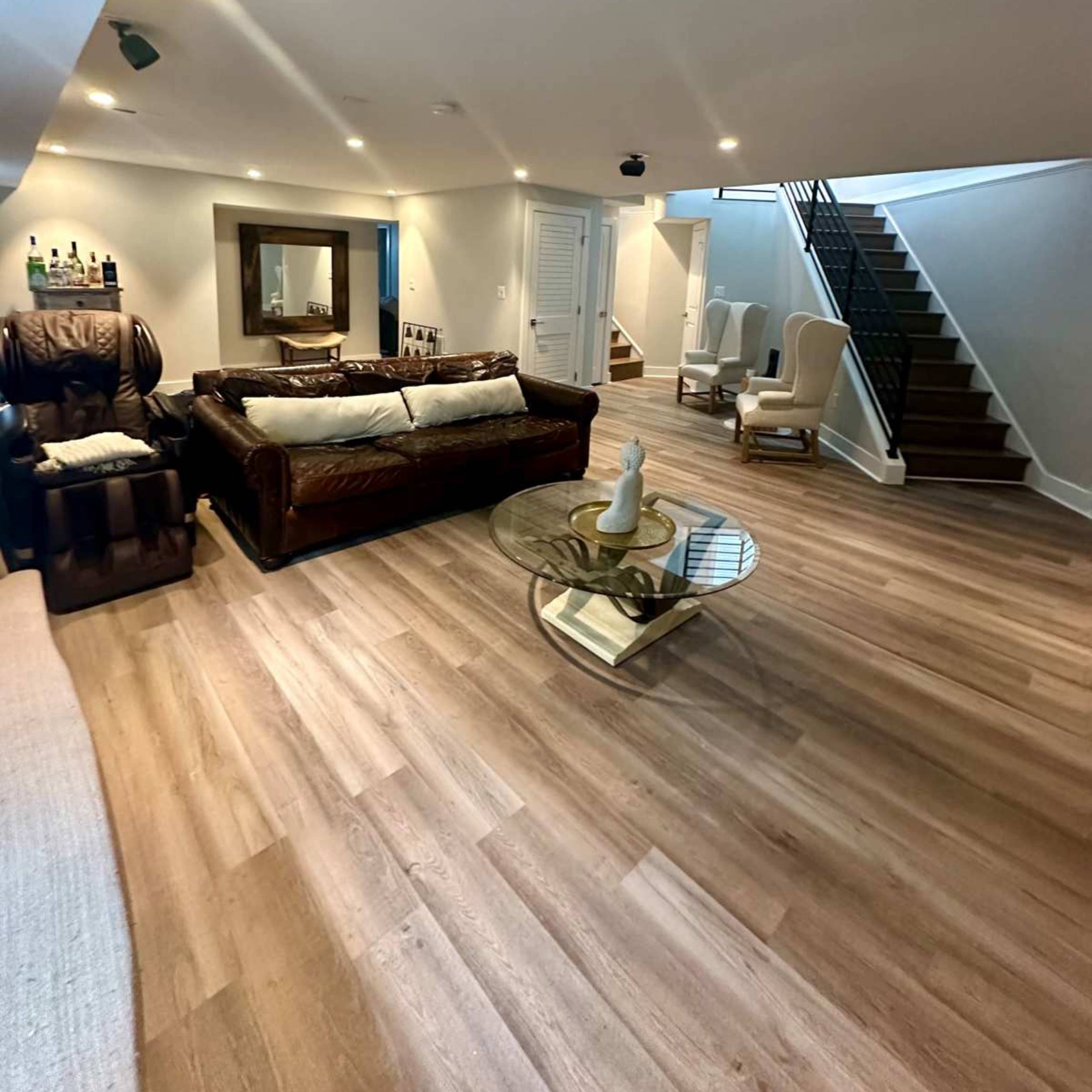 A finished basement with a sitting area featuring a leather couch, a glass coffee table, and a staircase leading to an upper level.