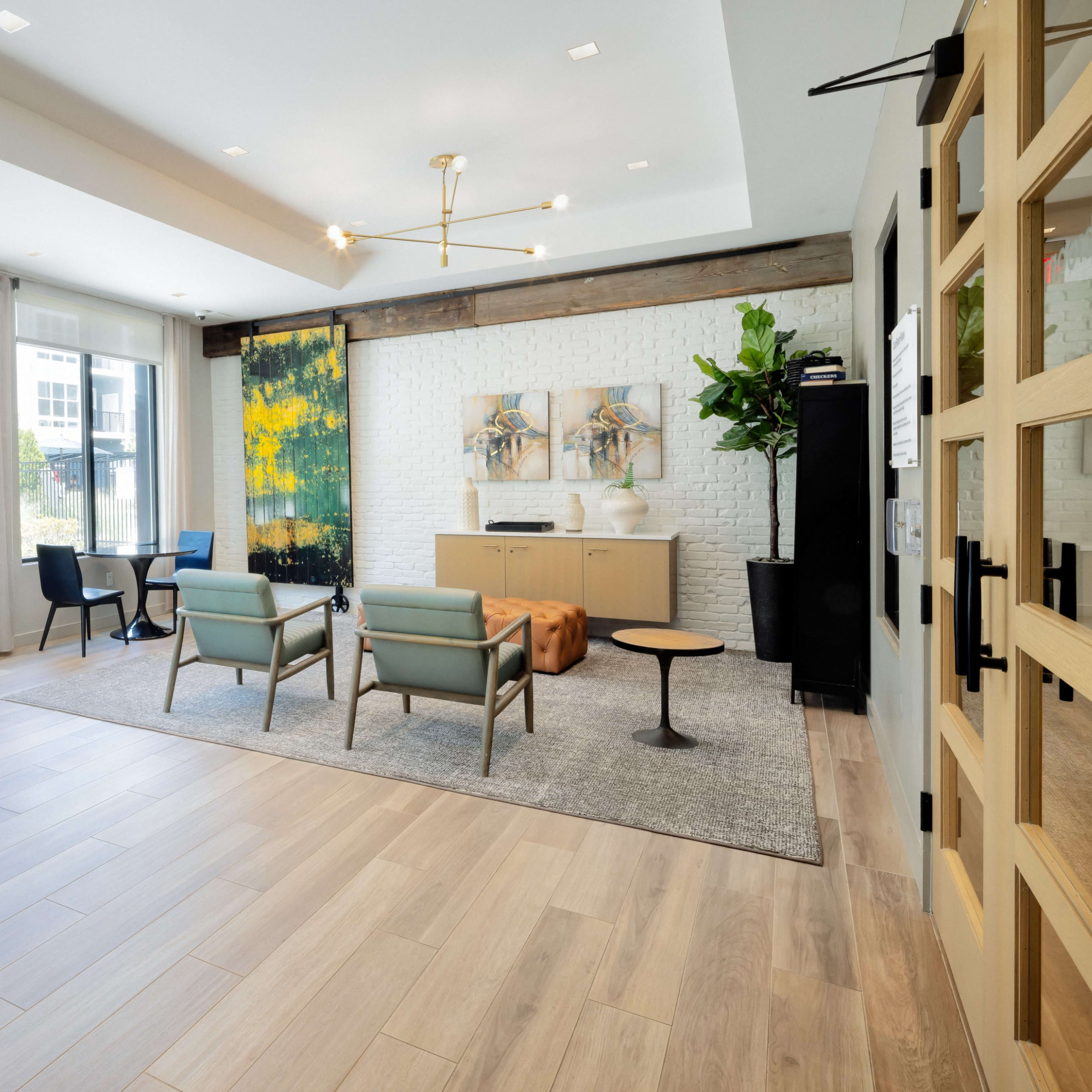 A modern lounge area with a seating arrangement, a coffee table, and a decorative wall art set against a bright, airy backdrop of large windows and wooden accents.