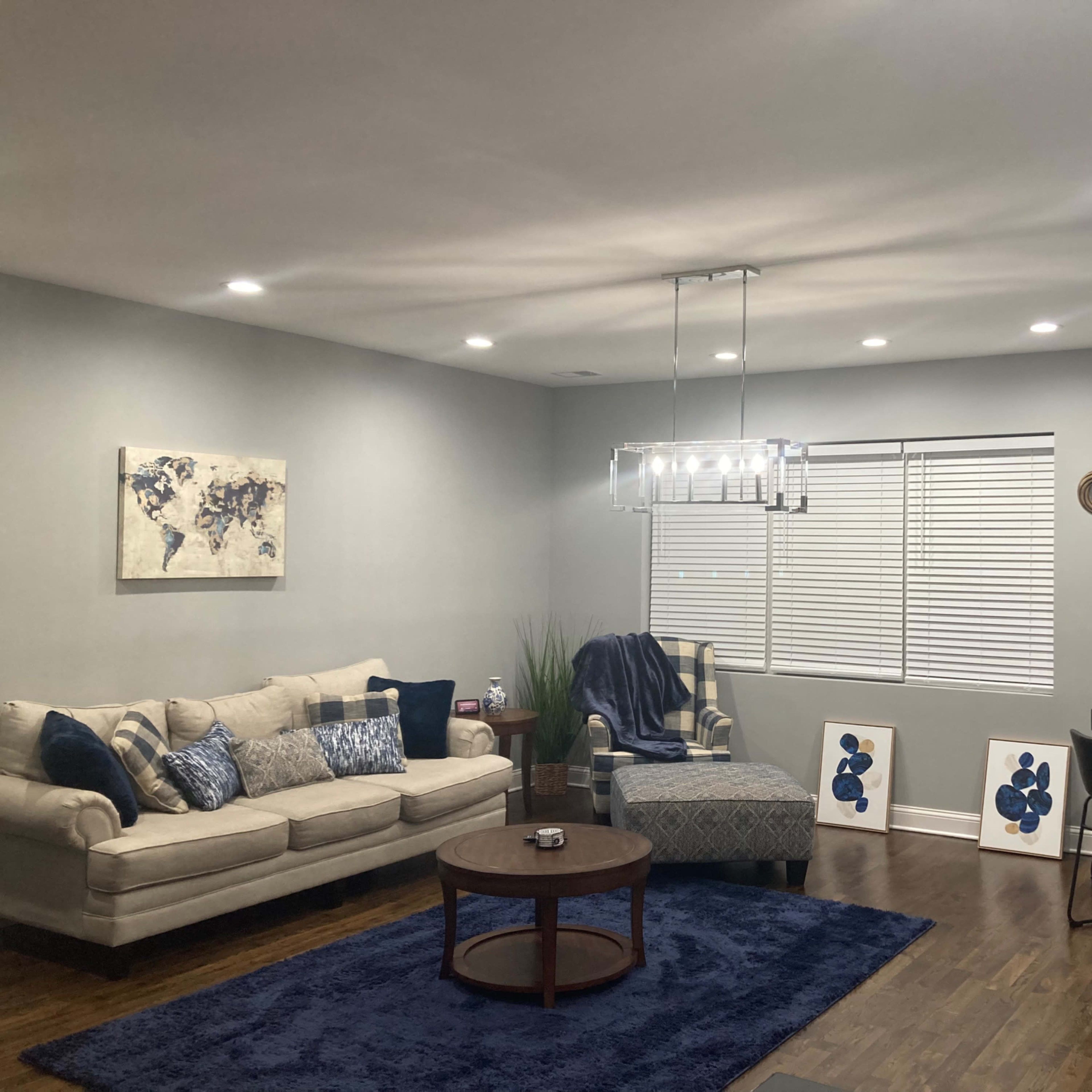 A modern living room with a beige sectional couch, a round wooden coffee table, a dining area with a black table and chairs, and decorative artwork on the walls.