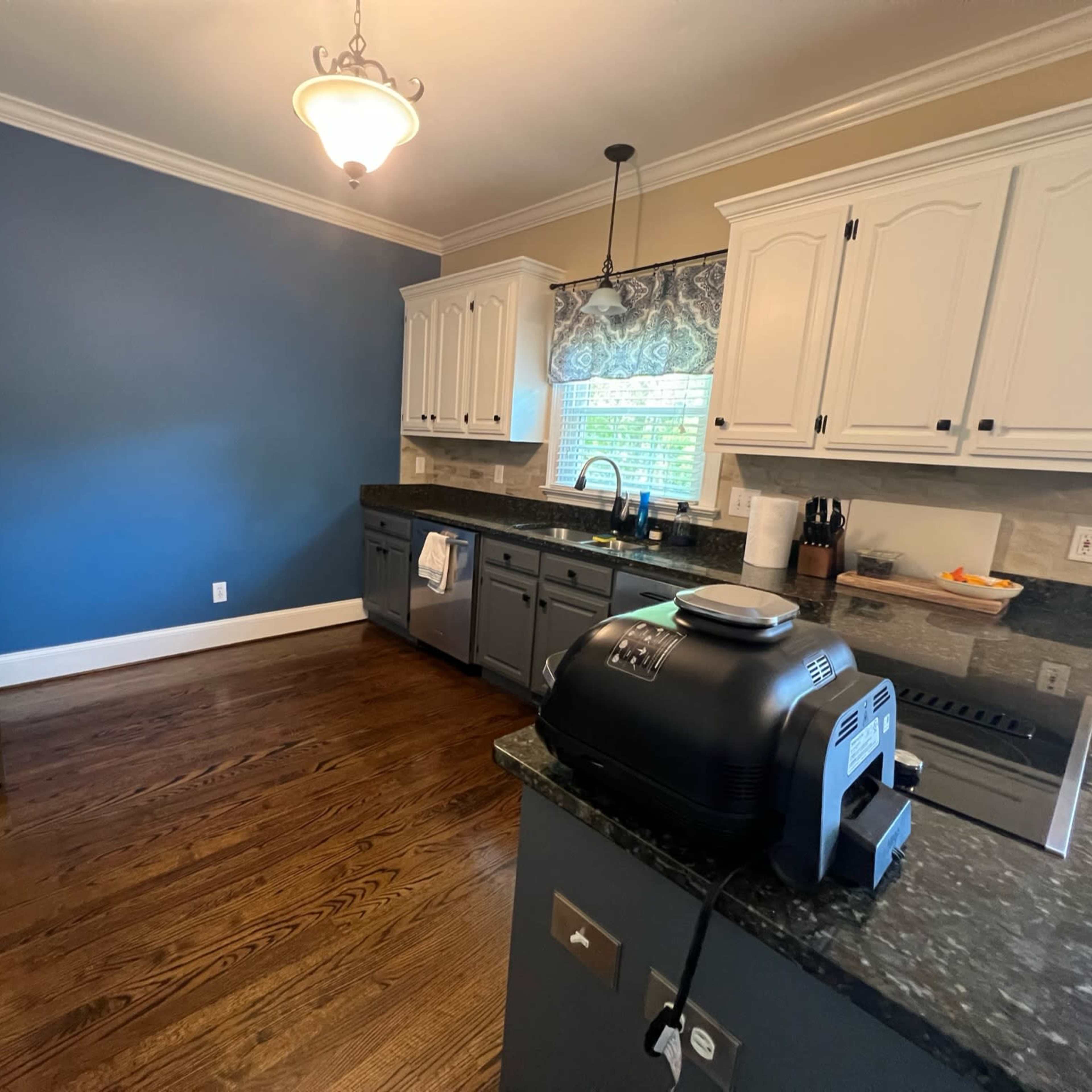 A kitchen features dark wood floors, white cabinetry, and a blue accent wall, with an air fryer on the countertop.