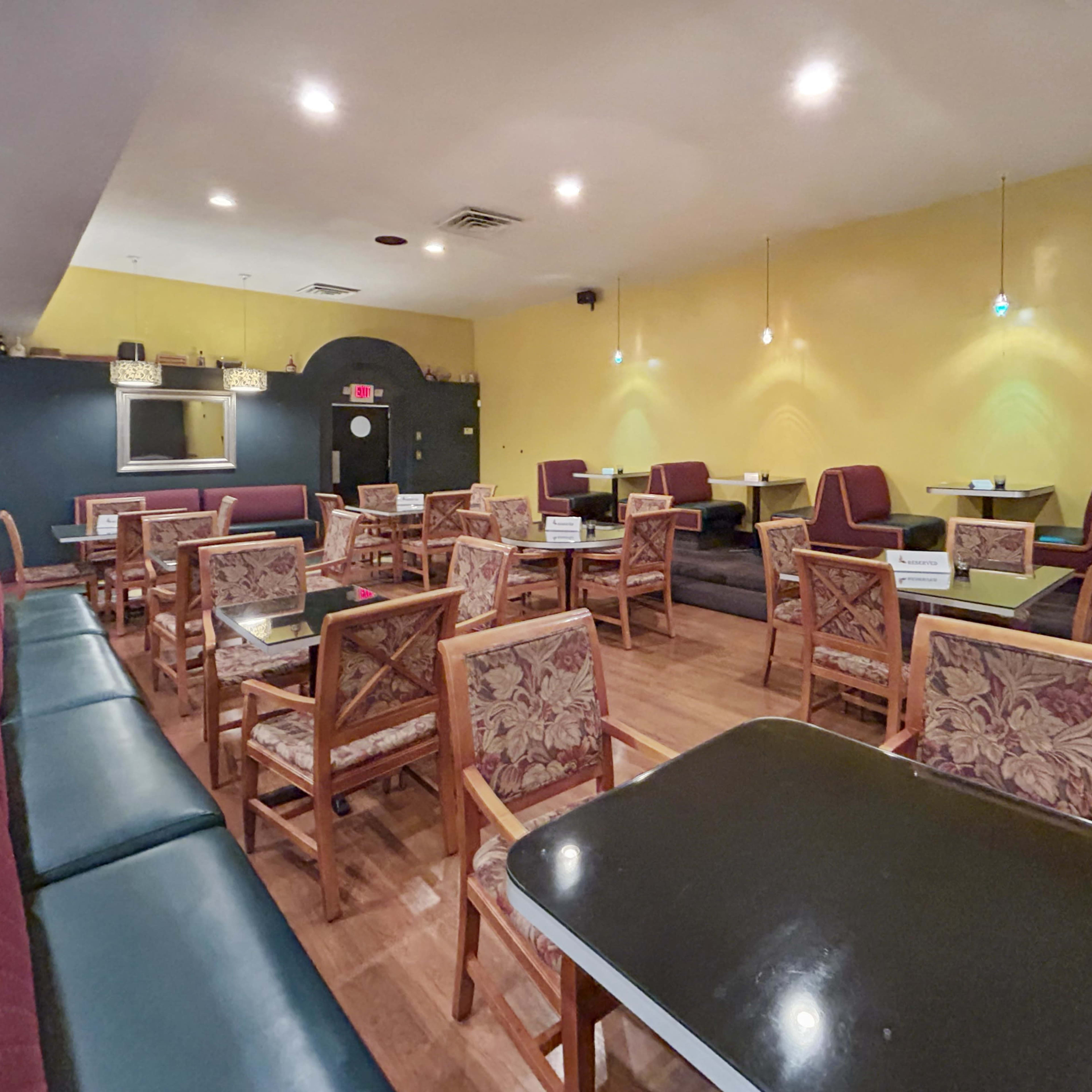 An empty cafe with wooden tables and chairs arranged on a patterned floor, and yellow walls adorned with wall lamps.
