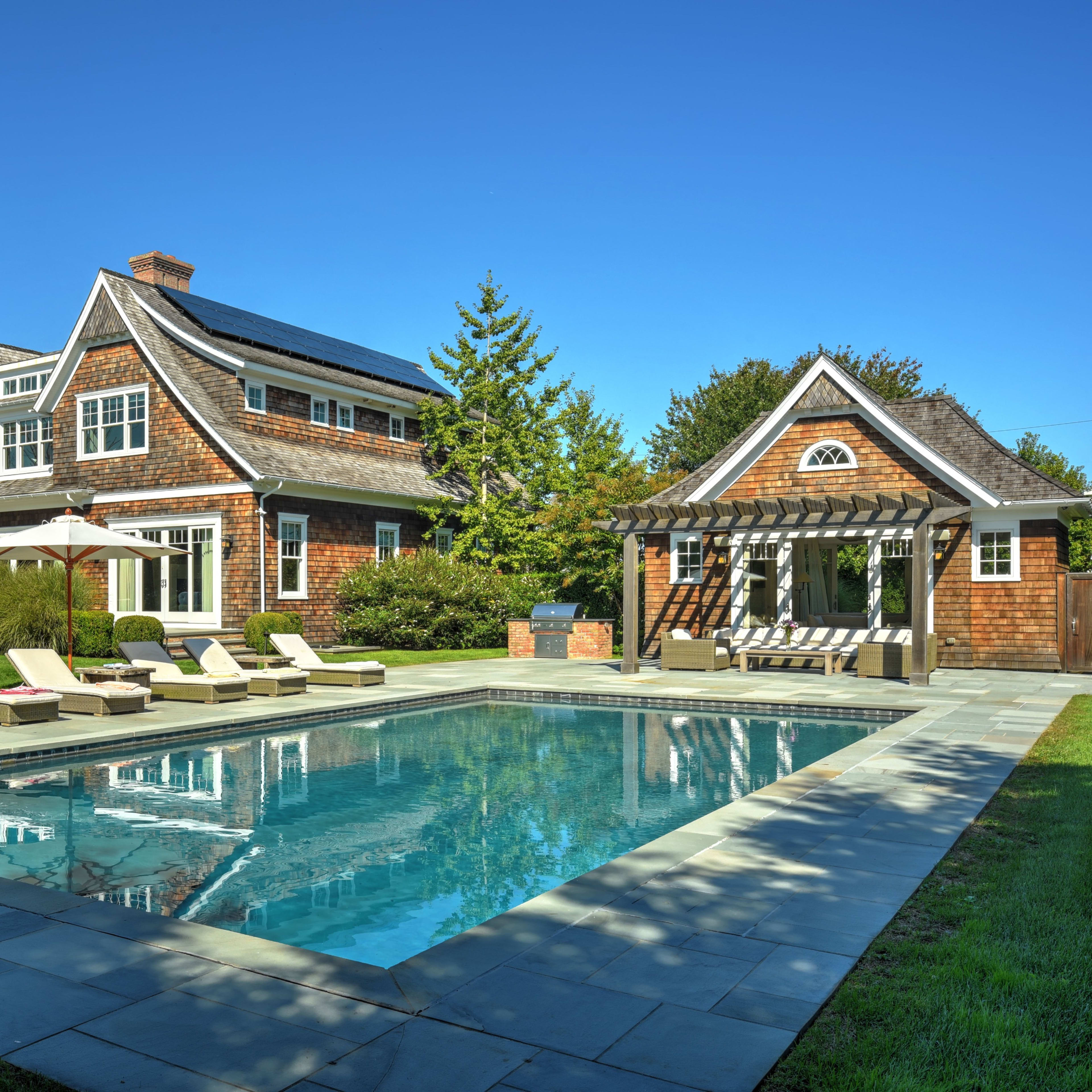 A two-story house with a pool and lounge chairs in a well-manicured yard.