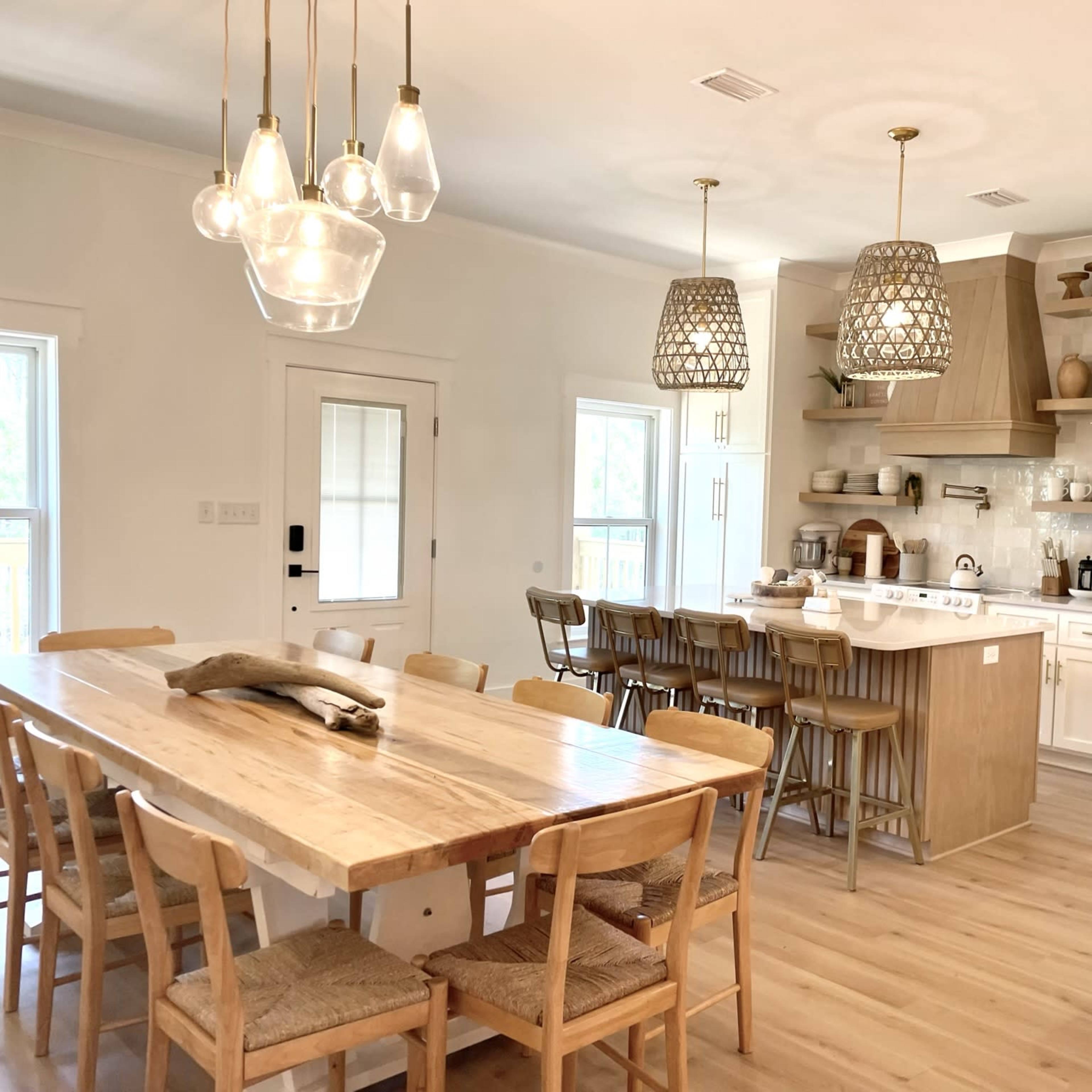 A modern kitchen and dining area featuring a large wooden table, several bar stools, and pendant lighting above the kitchen island.