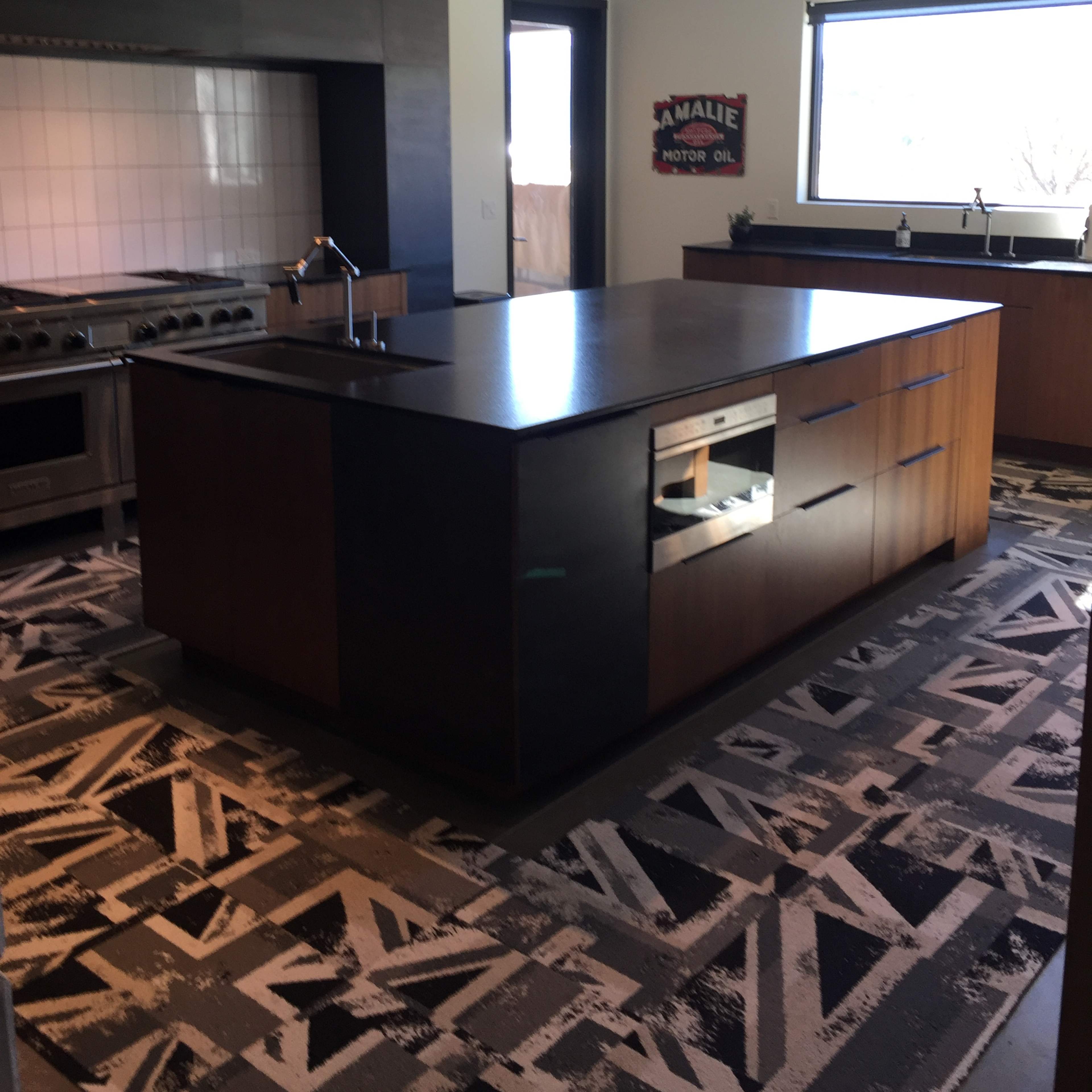 A modern kitchen with an island featuring a dark countertop, stainless steel appliances, and a patterned floor.