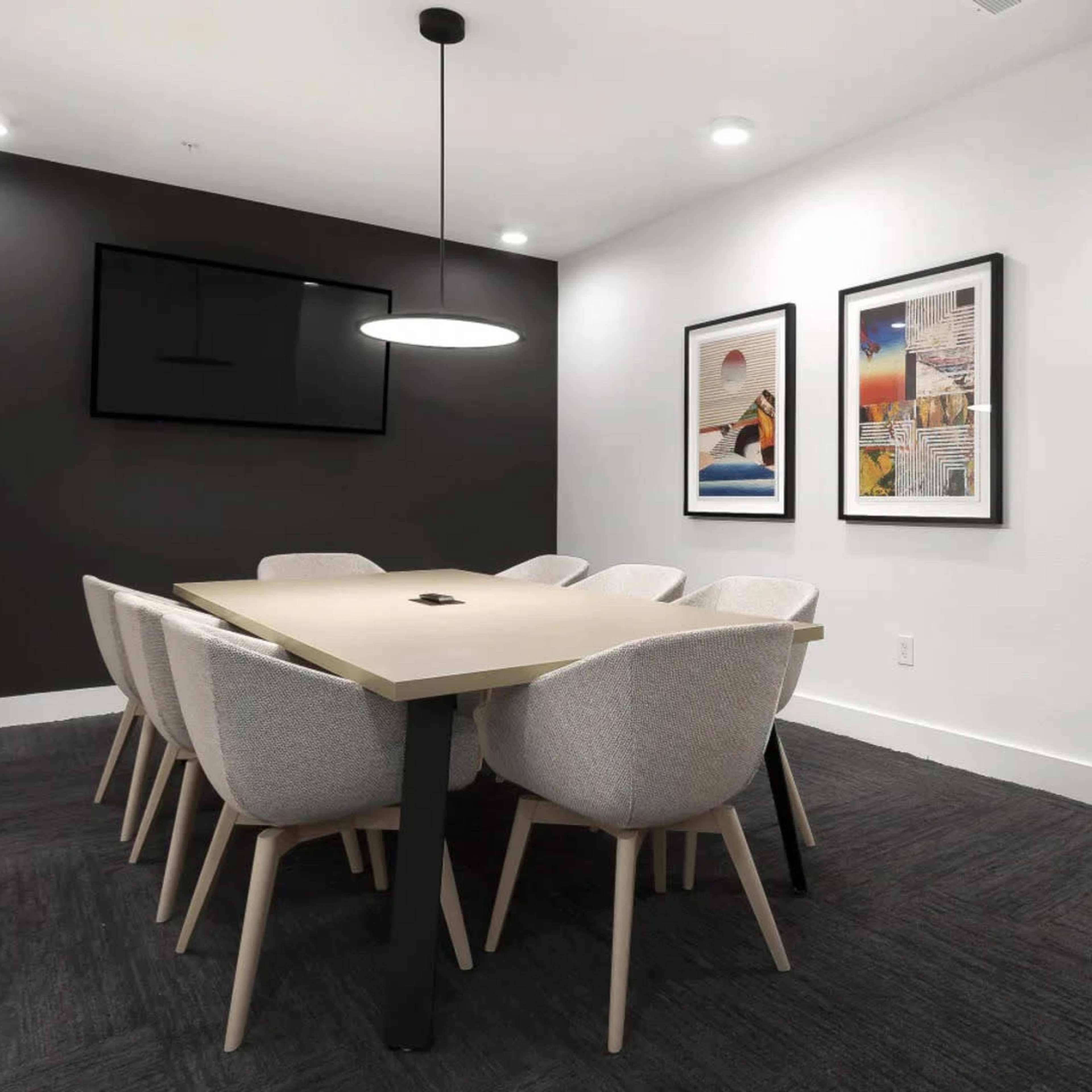 A modern conference room with a long table surrounded by eight upholstered chairs, flanked by black and white walls and two framed artworks.
