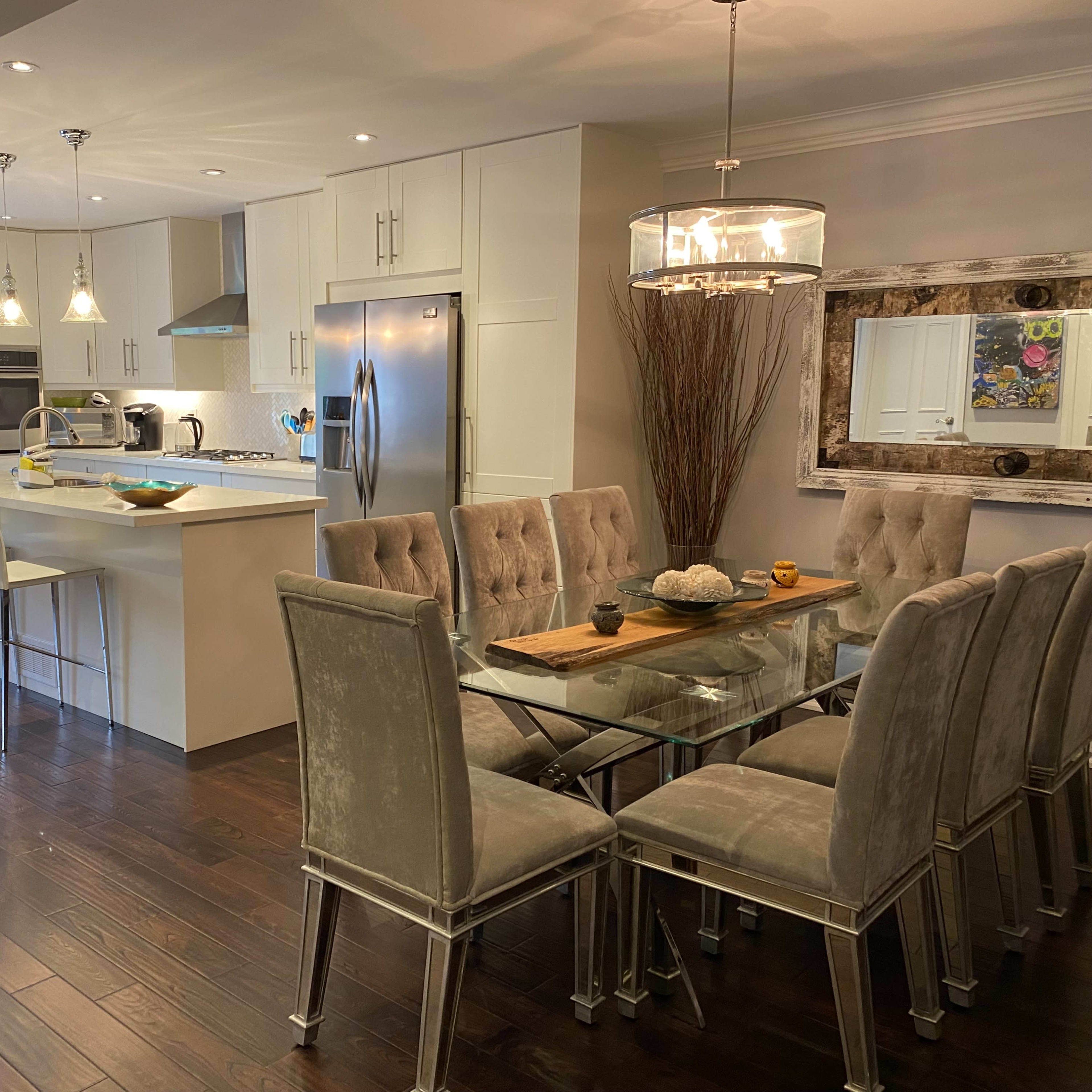 A modern kitchen and dining area with a glass dining table set for eight and a sleek kitchen with stainless steel appliances.
