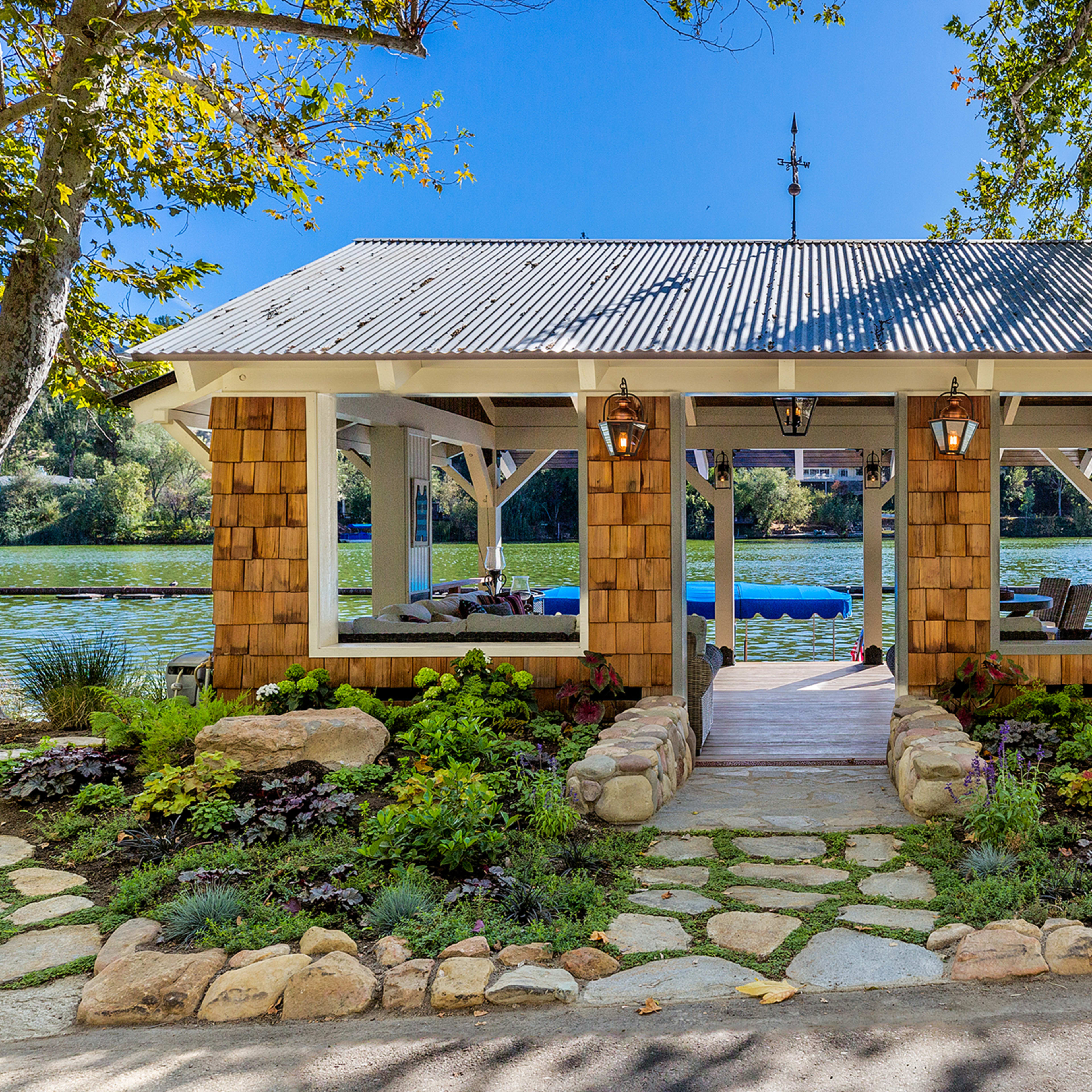 A lakeside gazebo with a stone walkway, surrounded by landscaped gardens and trees.