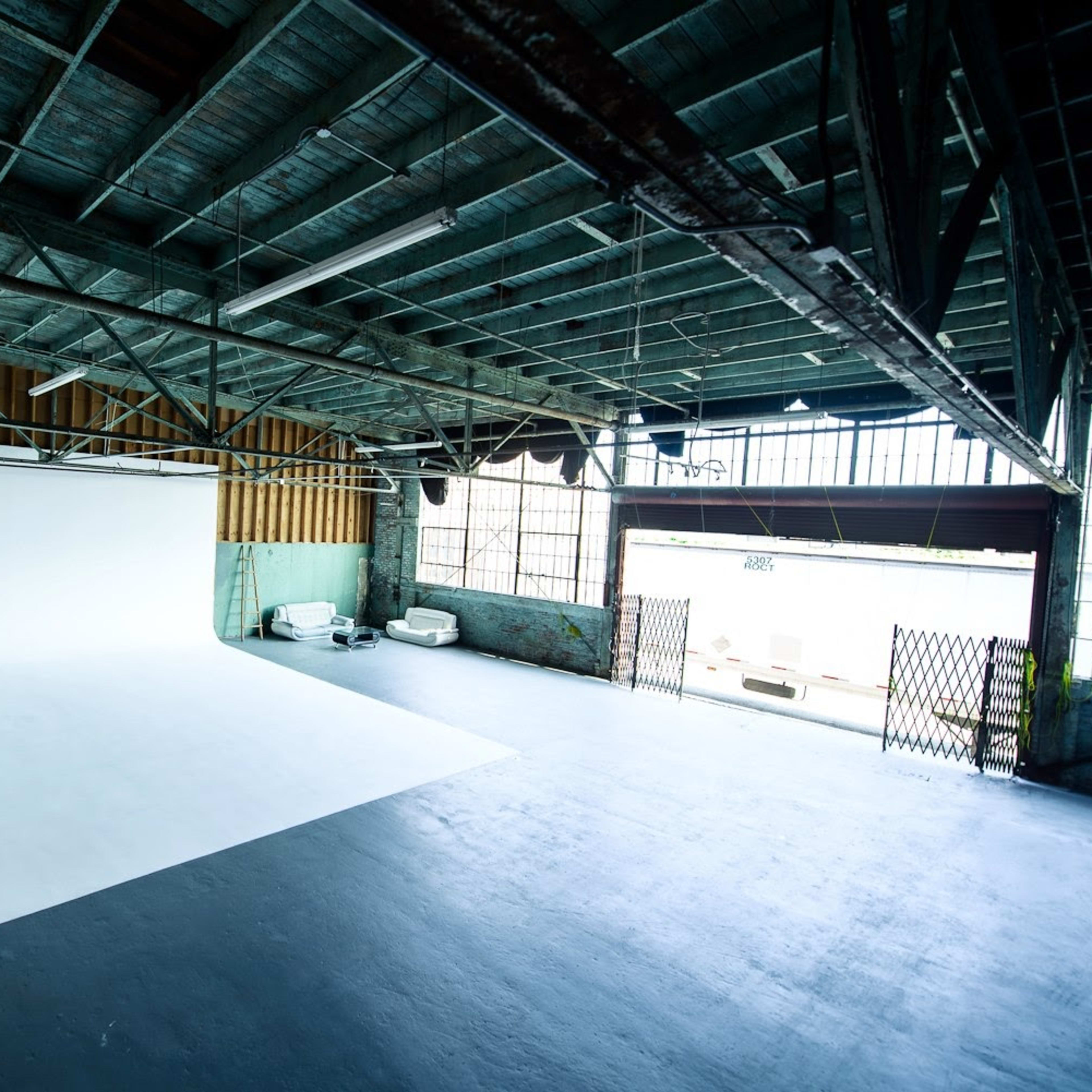 A spacious photography studio with a large white backdrop, exposed beams, and large windows letting in natural light.